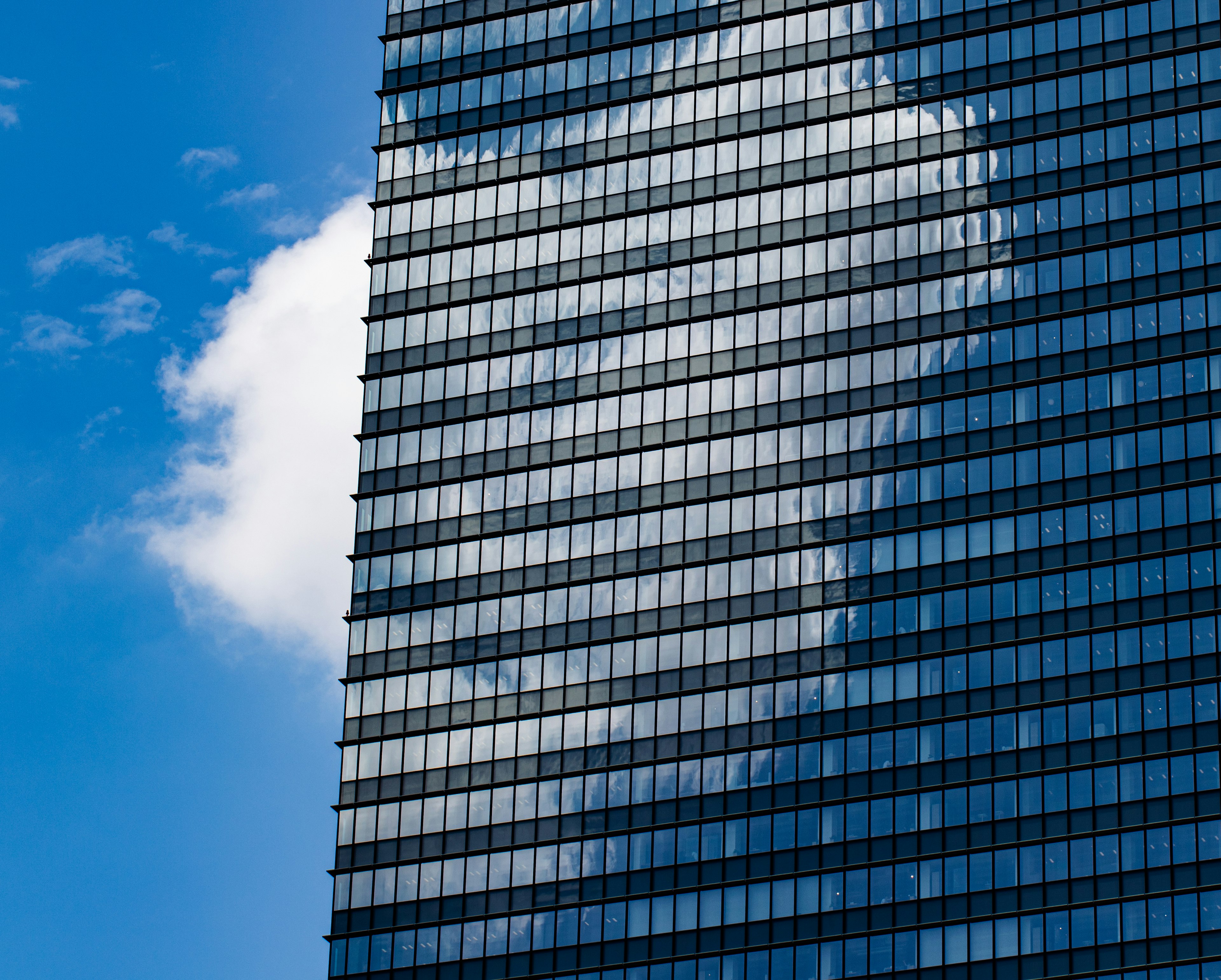 Glasfassade eines Hochhauses, die Wolken unter einem blauen Himmel reflektiert