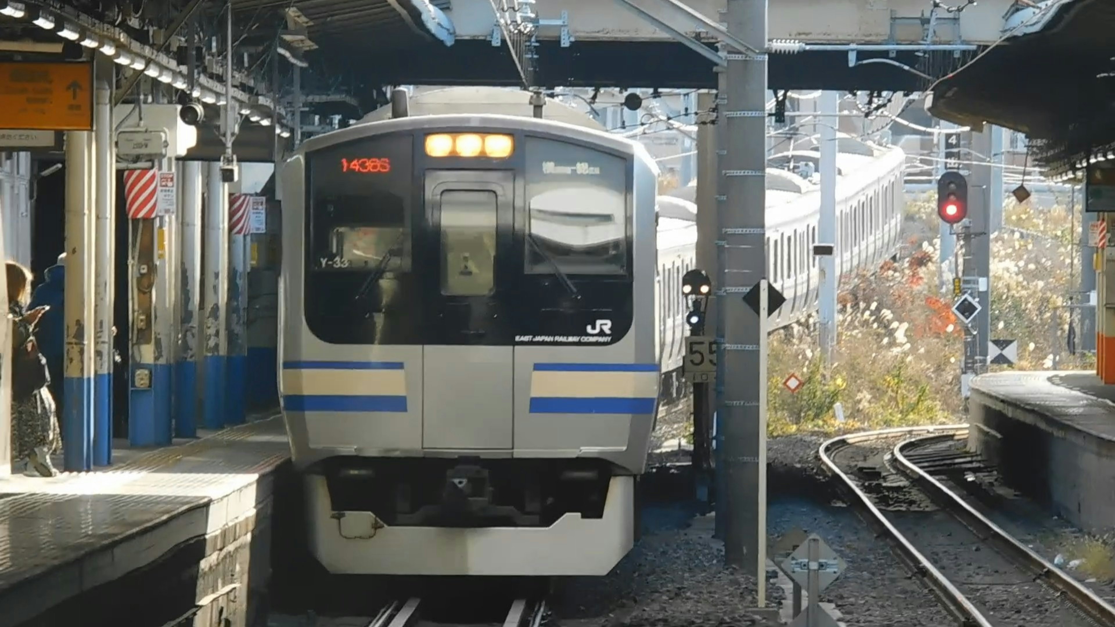 Train with blue stripes arriving at the station surrounded by people and signals