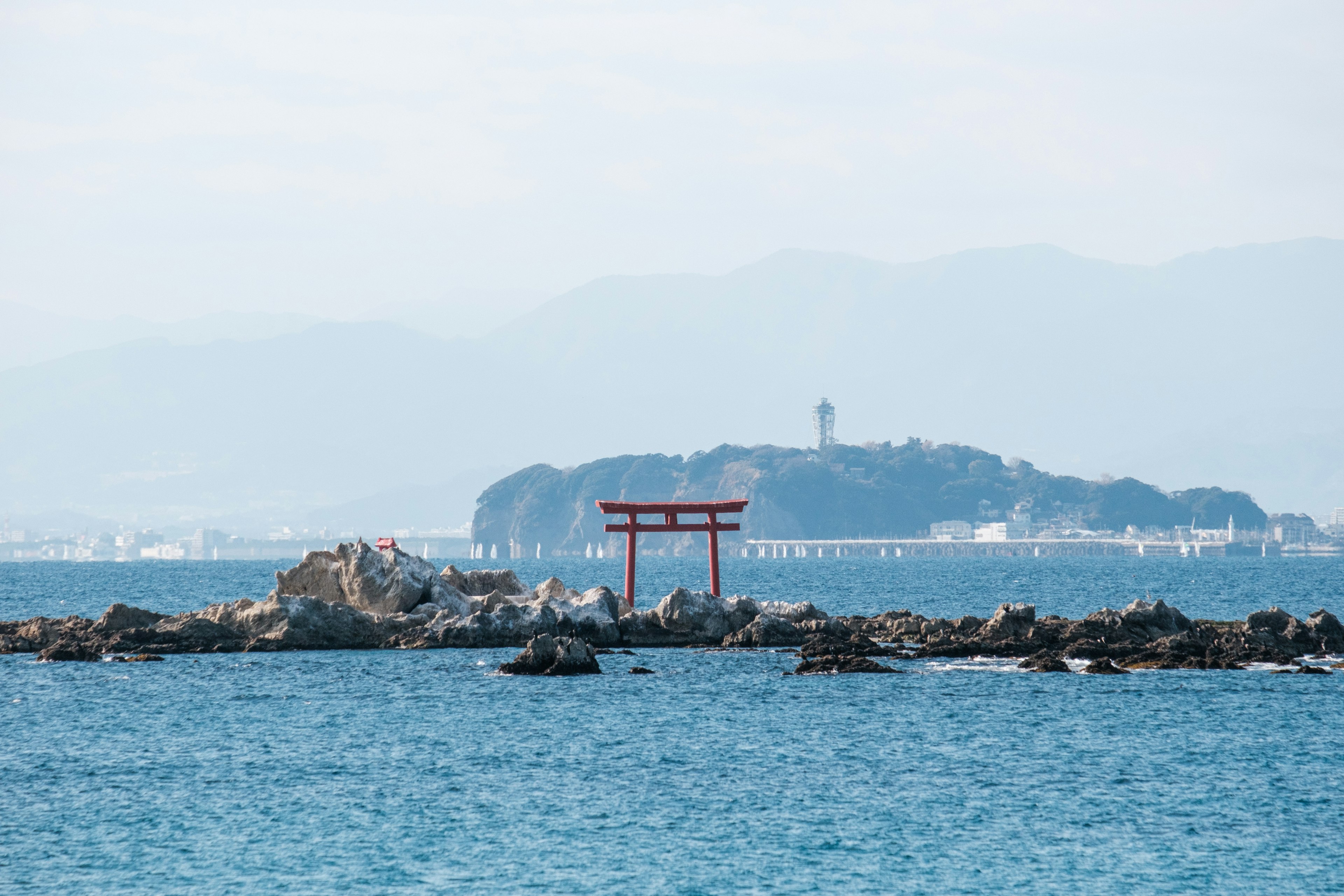 Torii in der Nähe des Meeres mit einer Insel im Hintergrund