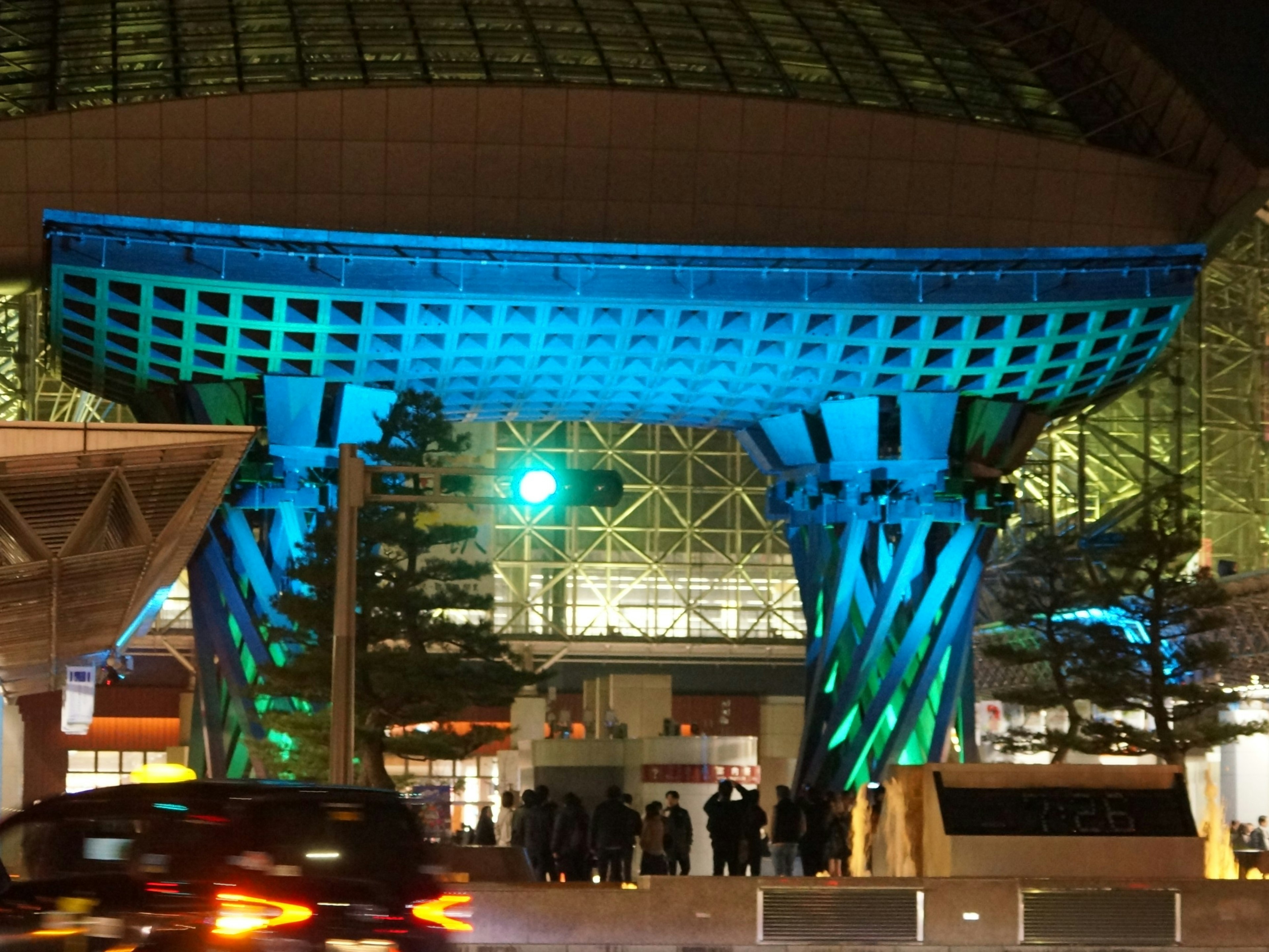 Entrada de un edificio iluminada por luces azules por la noche con personas