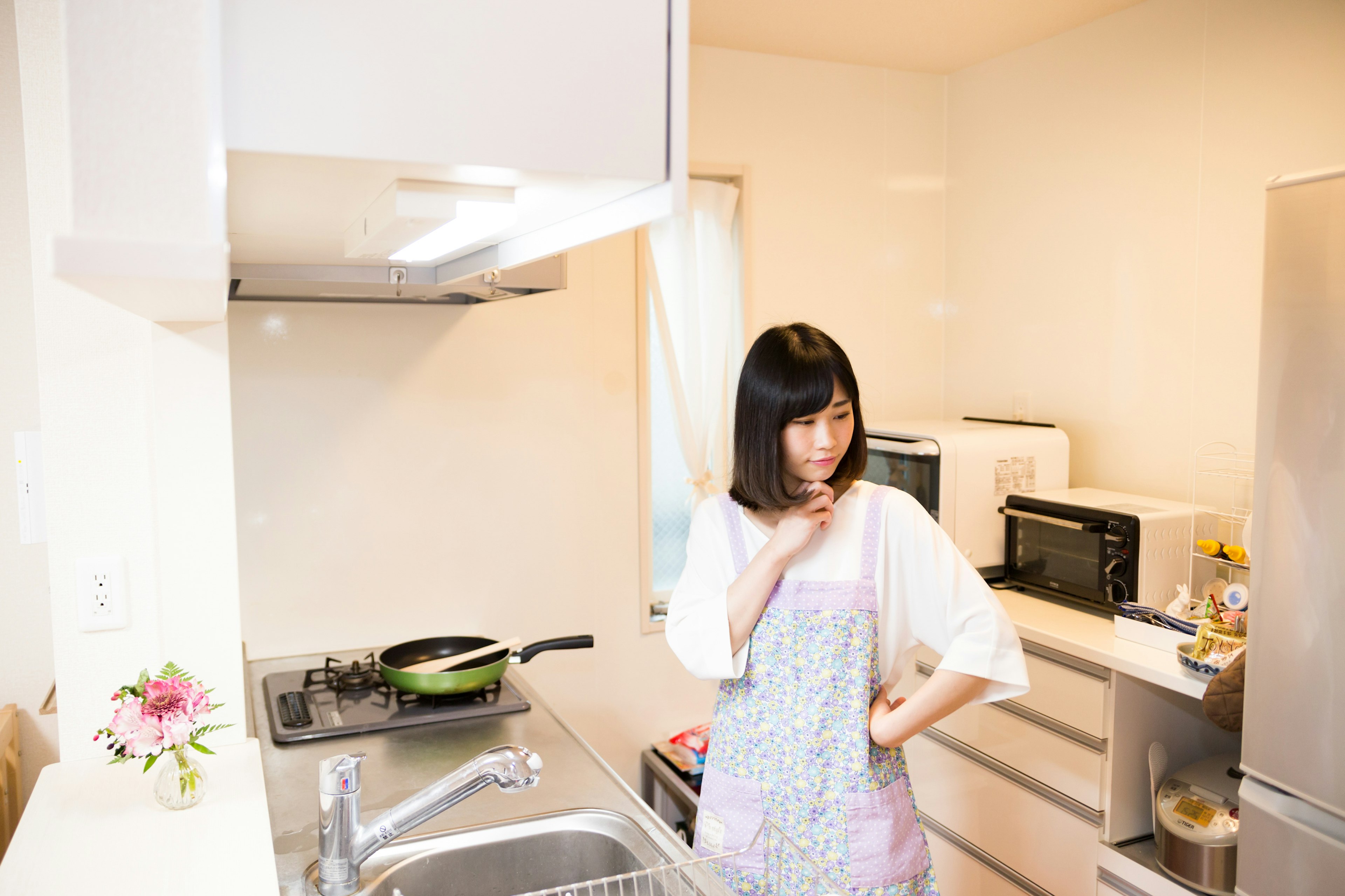 A woman pondering in a kitchen with a simple design featuring cooking utensils and microwaves