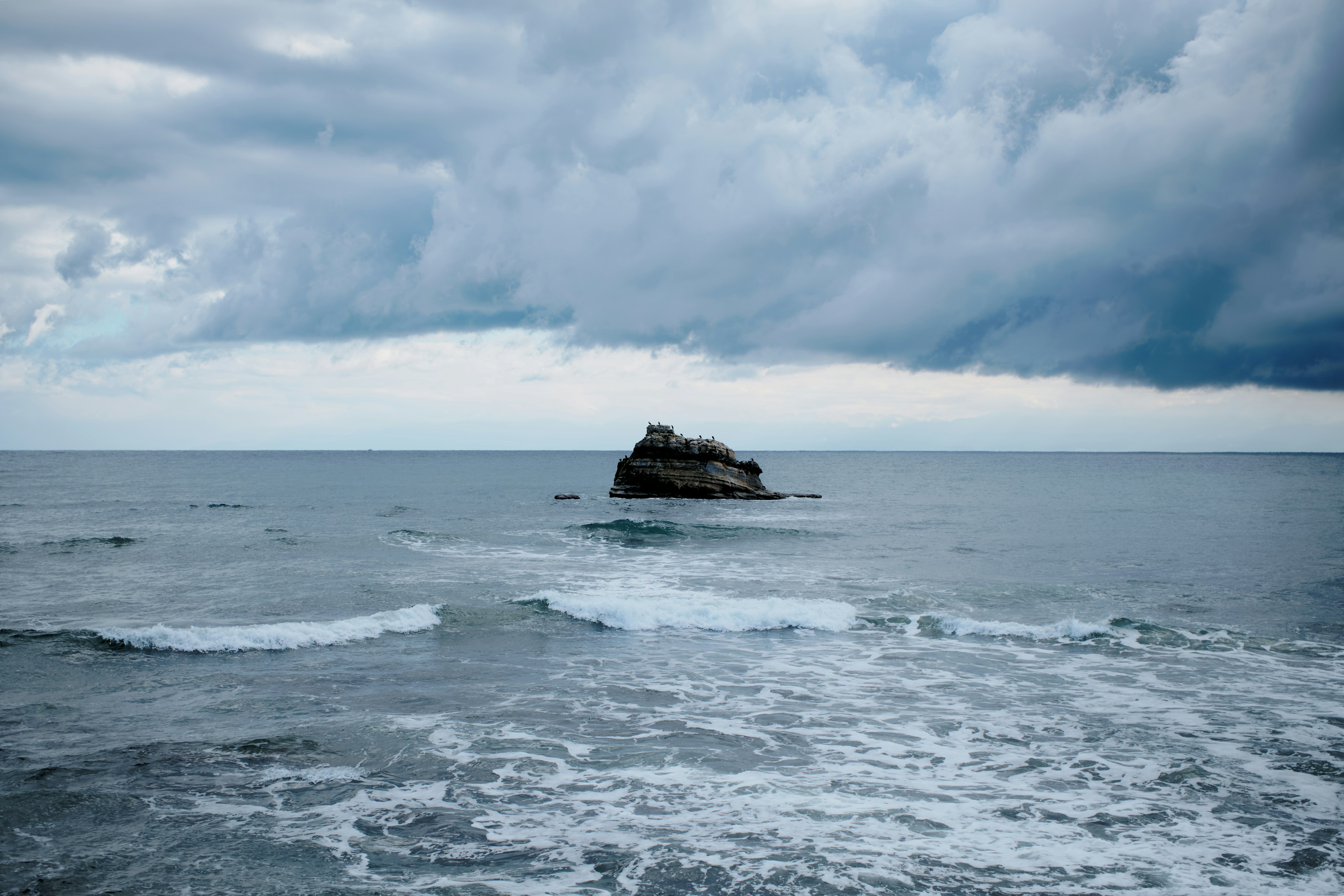 Sebuah pulau batu kecil di lautan di bawah langit mendung