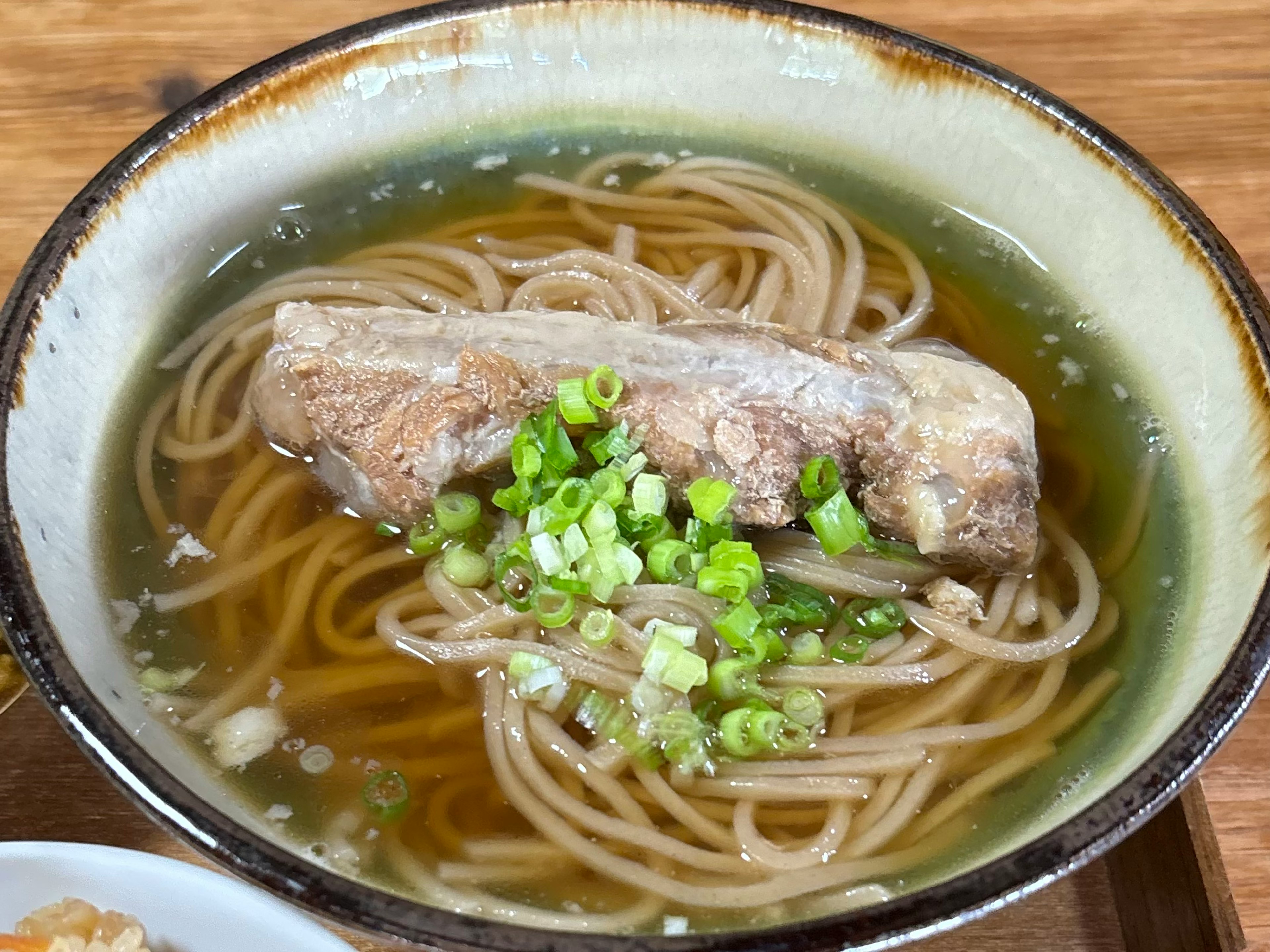 Mangkuk mie soba dalam kaldu jernih dengan irisan bawang hijau dan potongan ikan