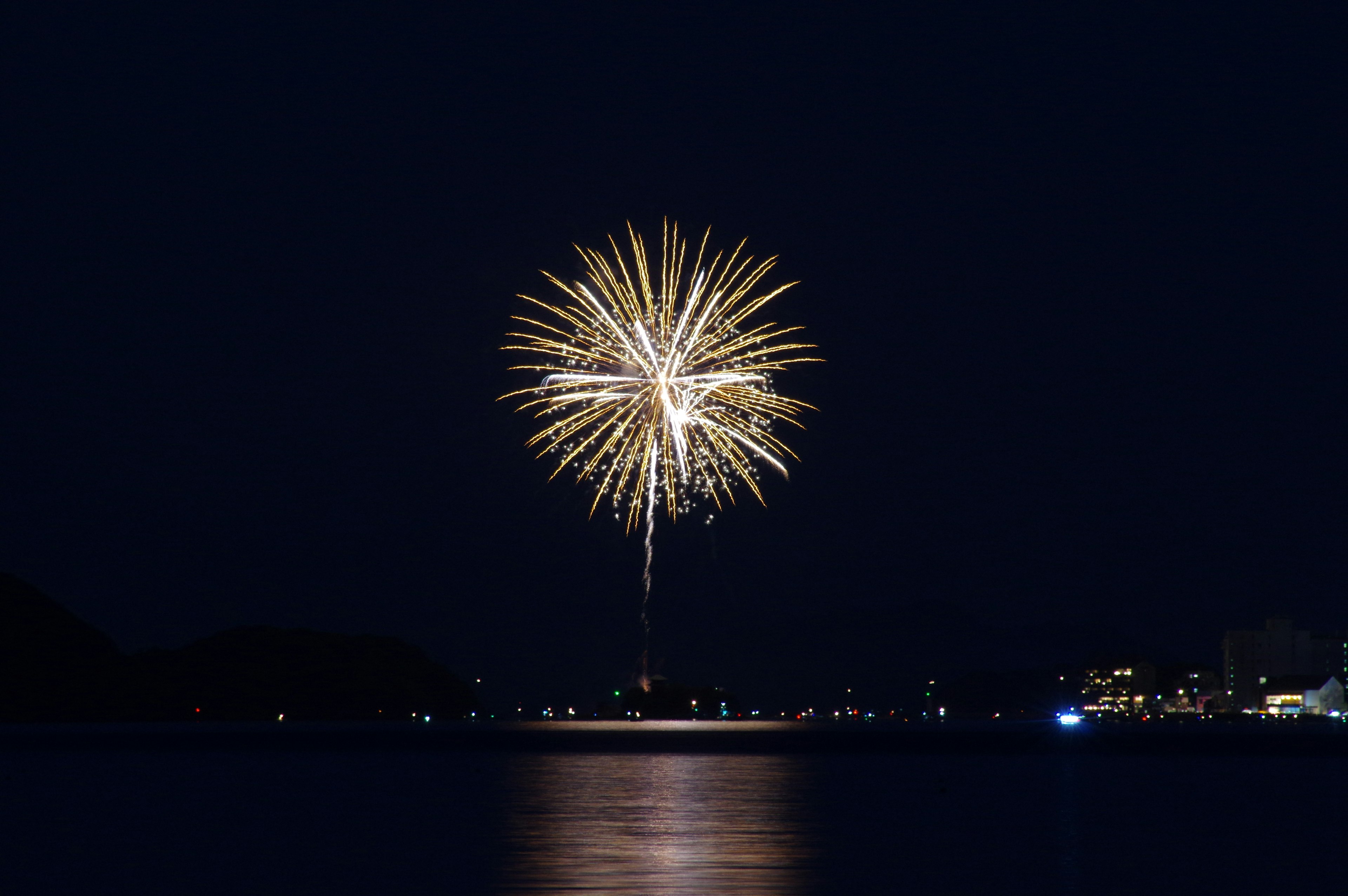 Un impresionante fuego artificial estallando en el cielo nocturno reflejado en el agua