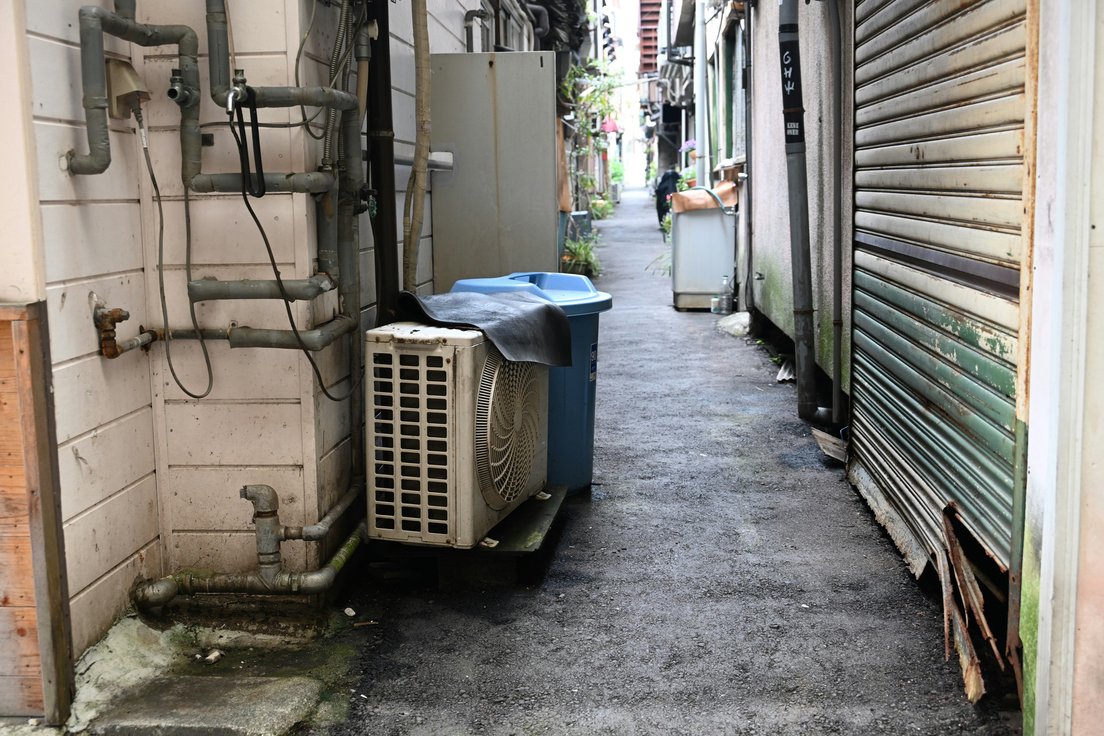 狹窄的小巷裡有一個藍色的垃圾桶和一個空調外機