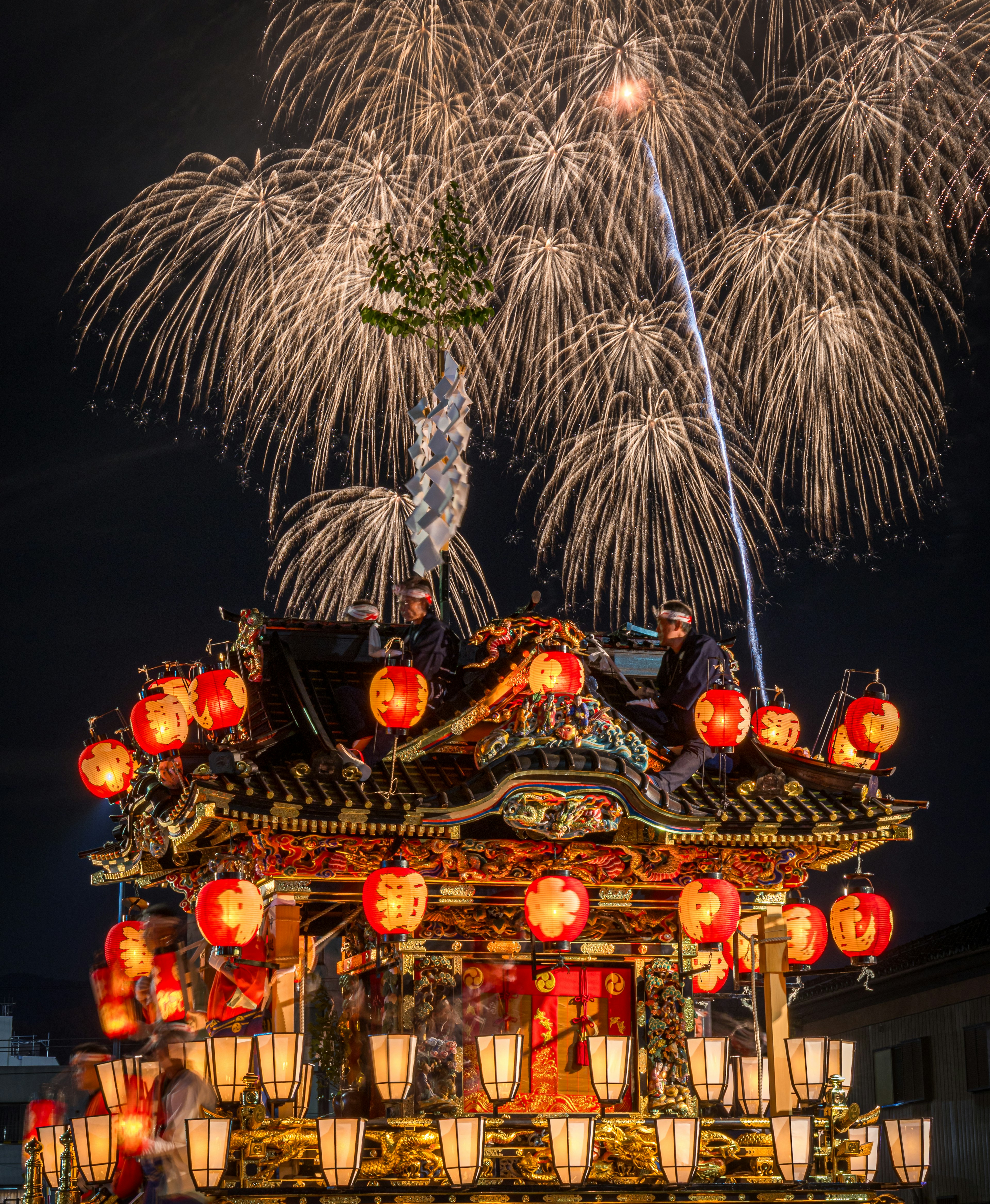 Festive float adorned with lanterns illuminated against a backdrop of fireworks in the night sky