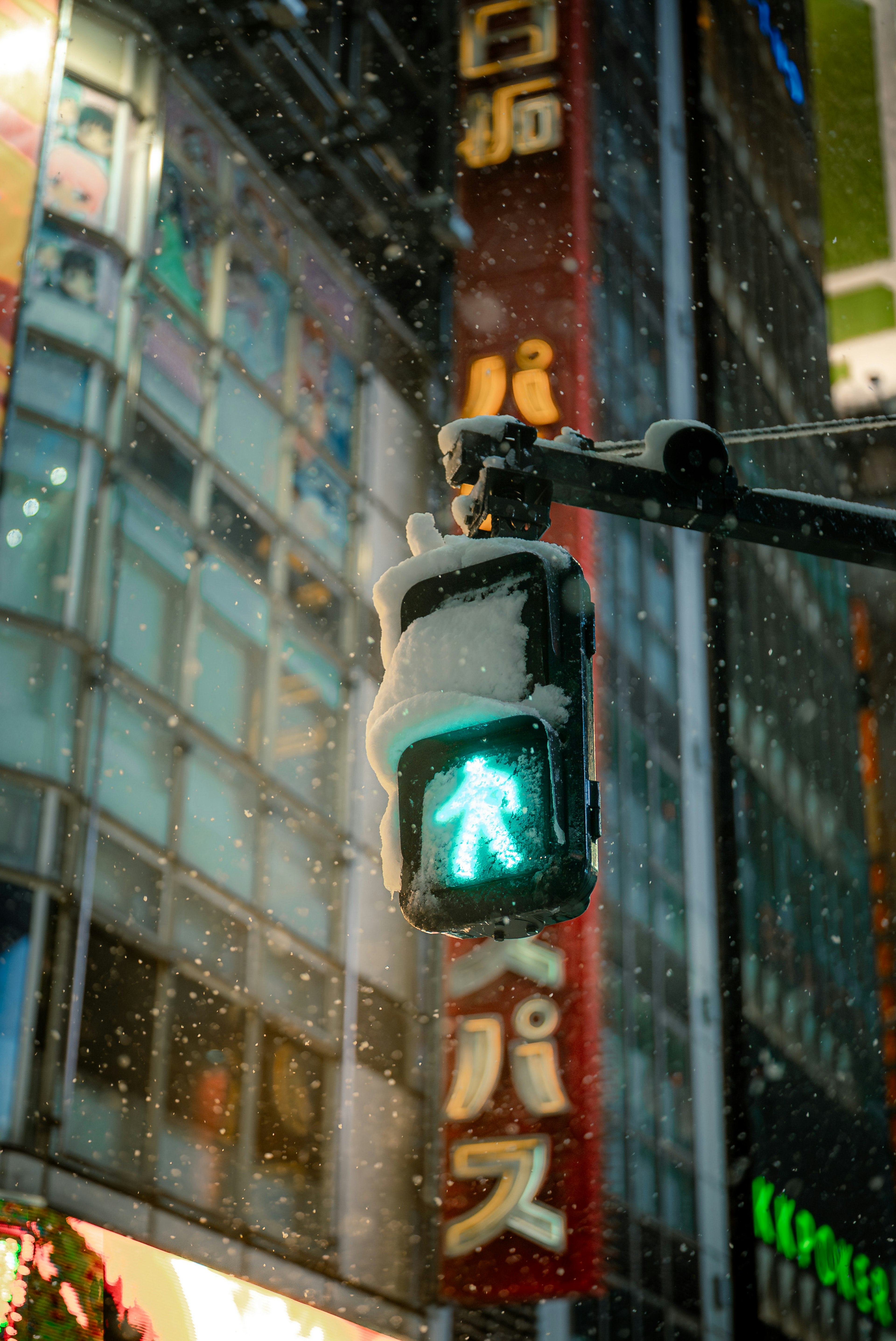 Green pedestrian signal illuminated in snowfall with neon signs in the background