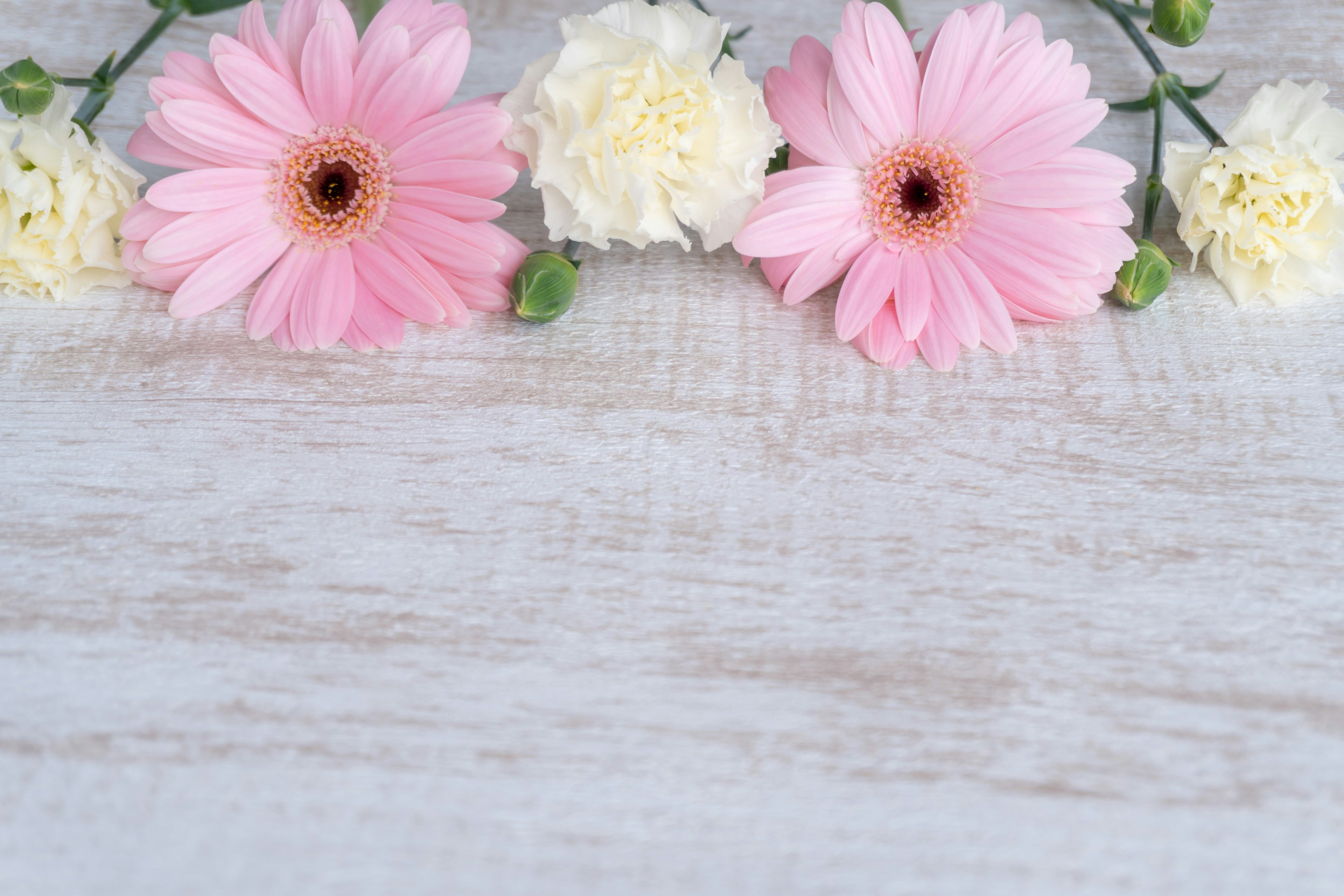 Image of pink flowers and white carnations arranged on a wooden surface