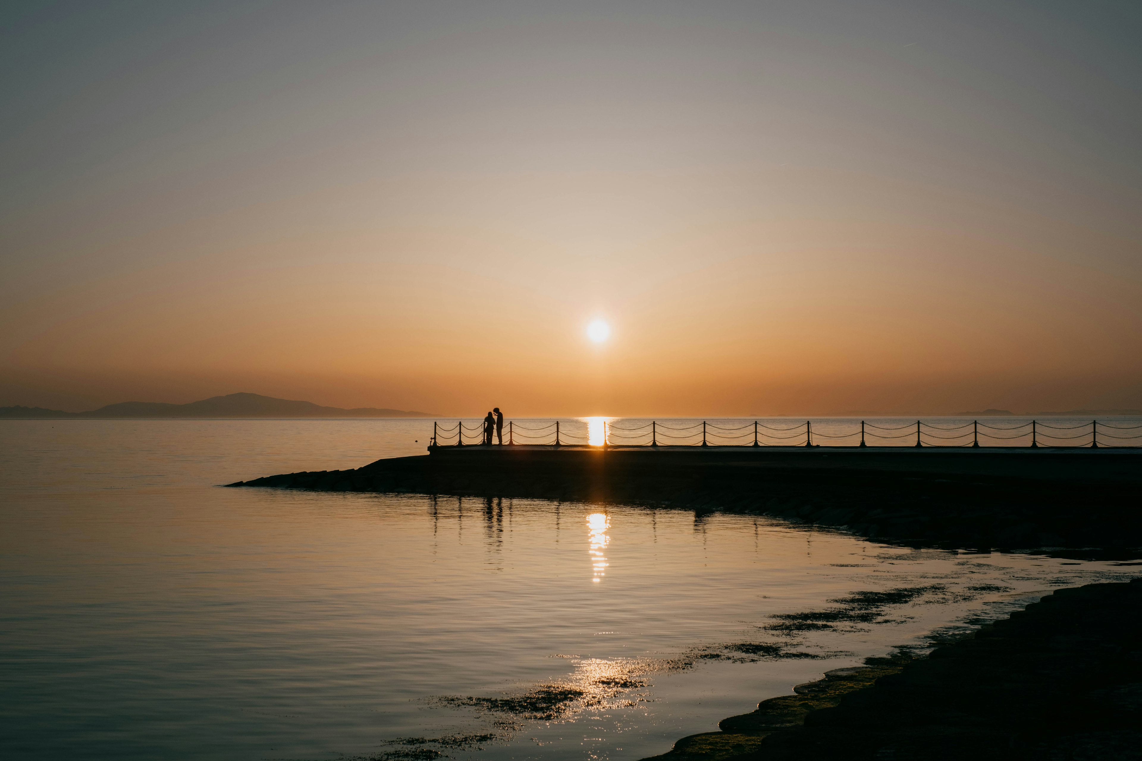 Puesta de sol sobre aguas tranquilas siluetas de personas en la orilla