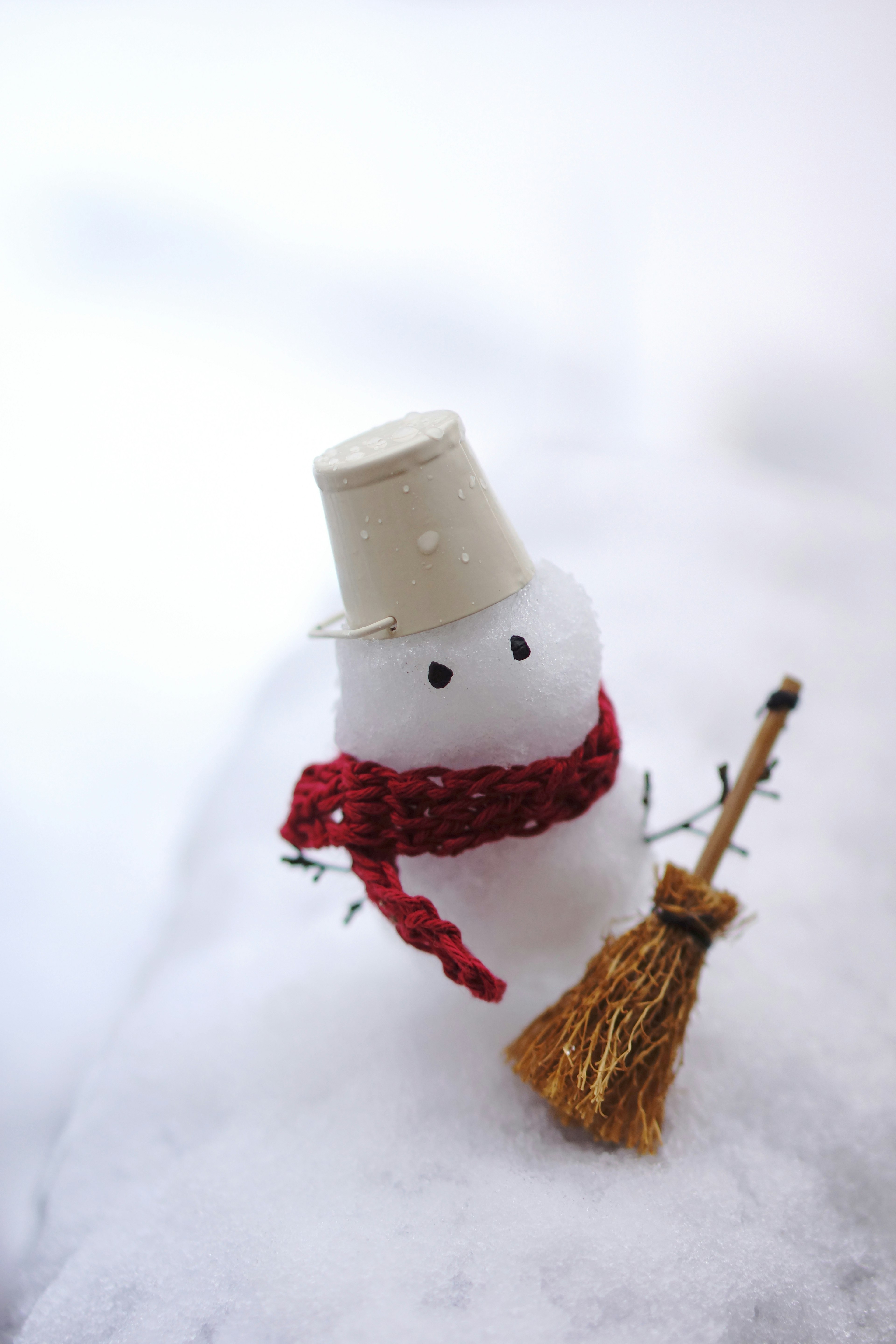 A snowman wearing a red scarf and a white hat standing on white snow