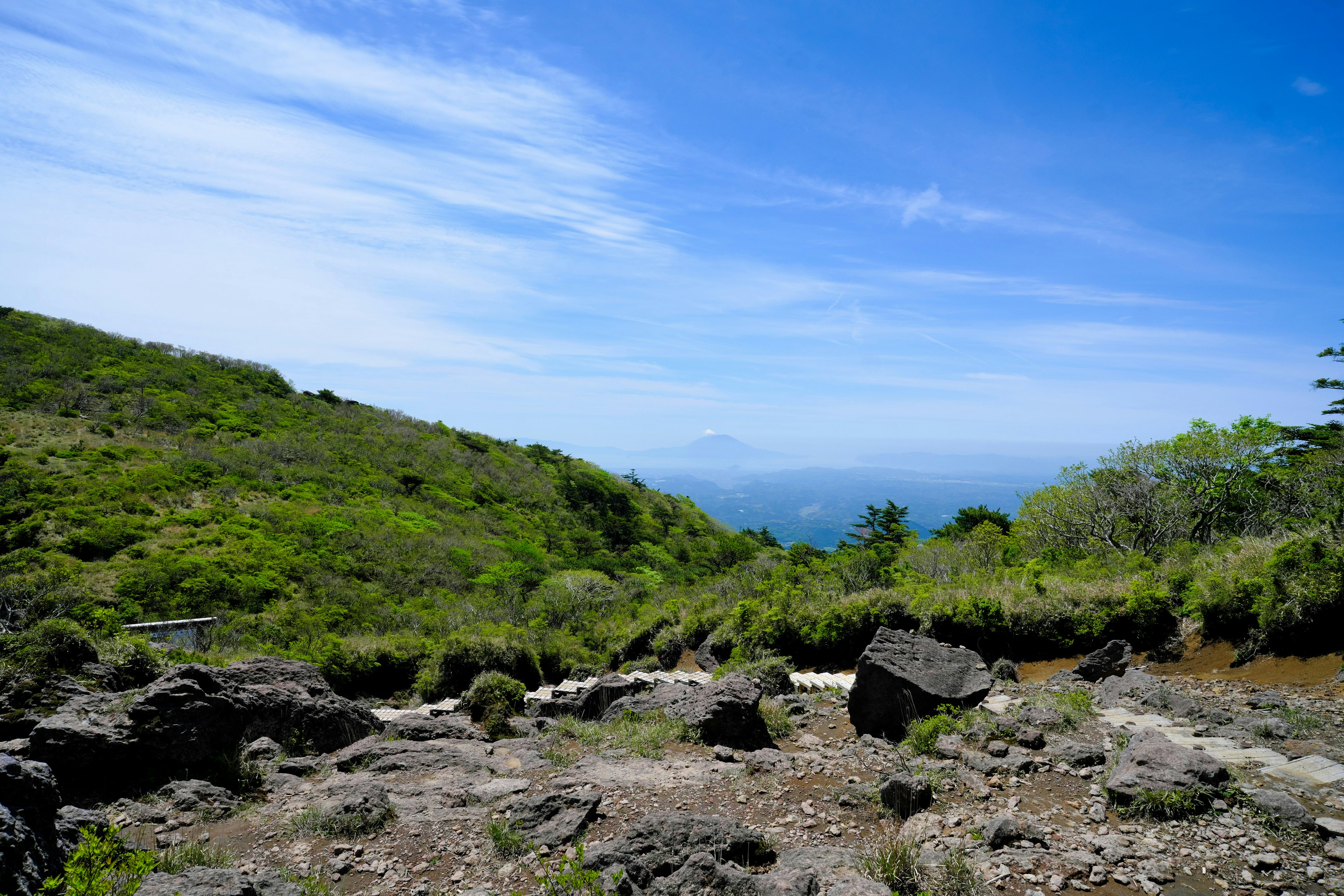 Lush green mountain landscape under a blue sky featuring rocky terrain and distant mountains