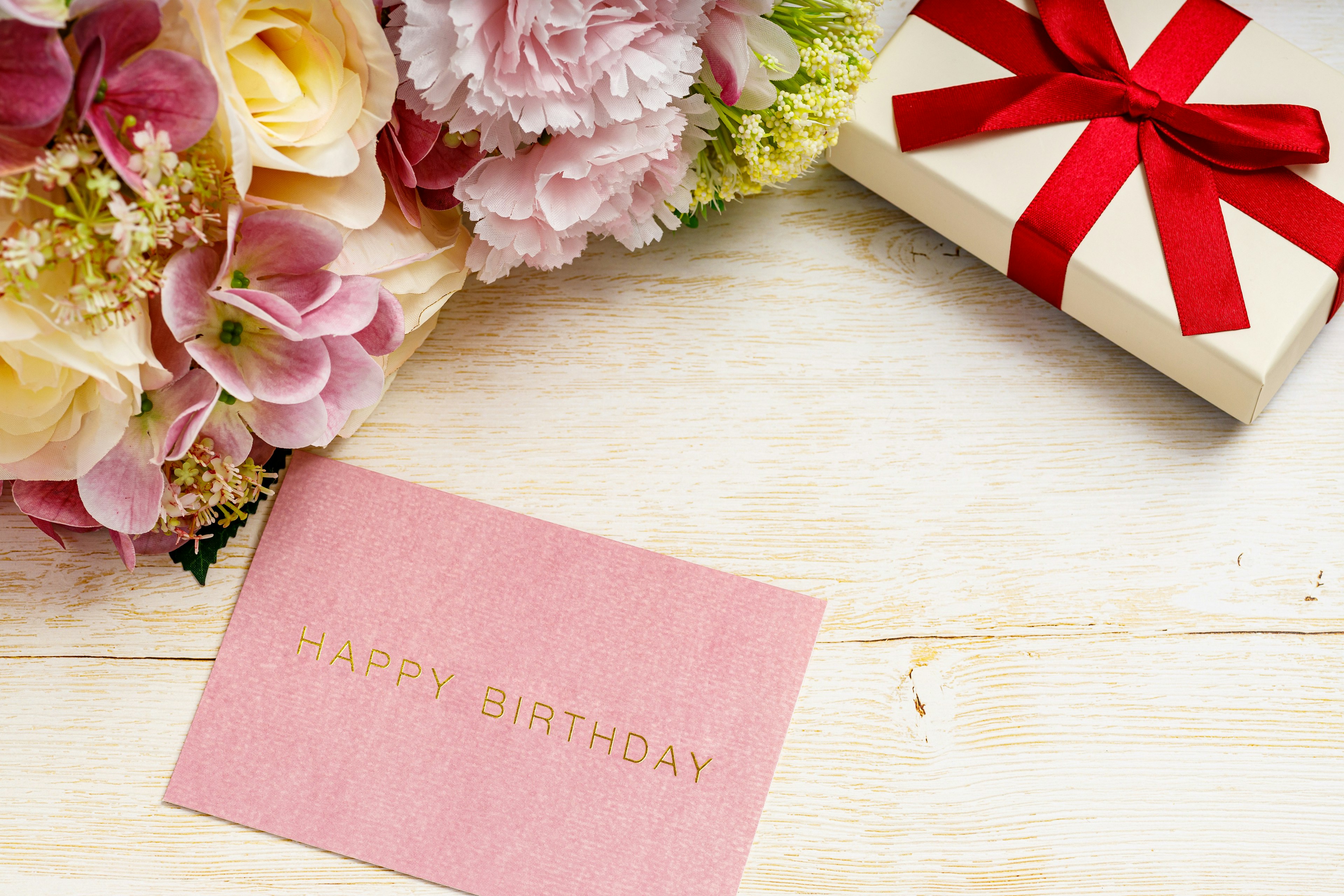 Tarjeta de cumpleaños rosa con flores y una caja de regalo con un lazo rojo