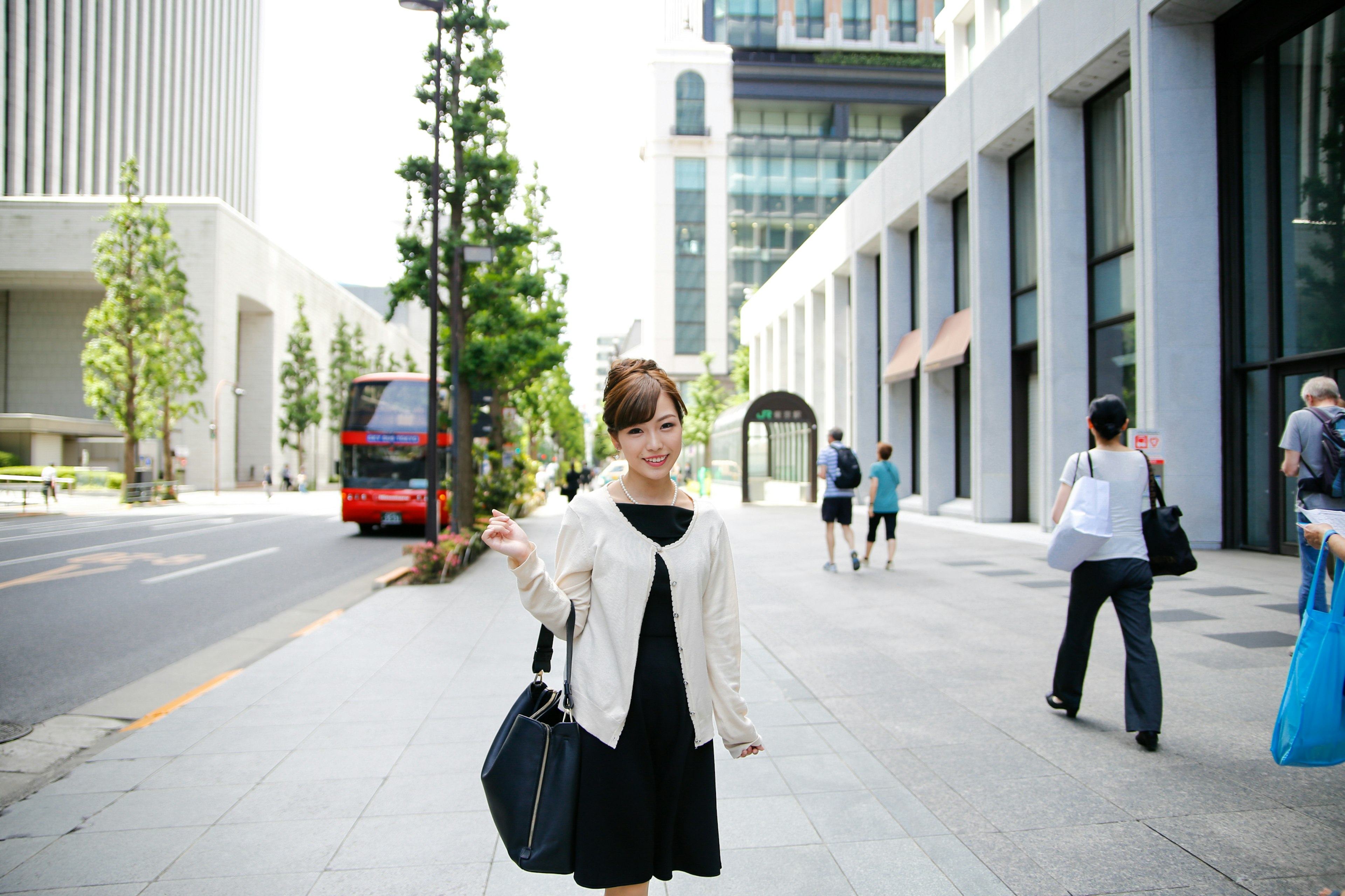 A woman in a black dress wearing a white jacket stands on a city street