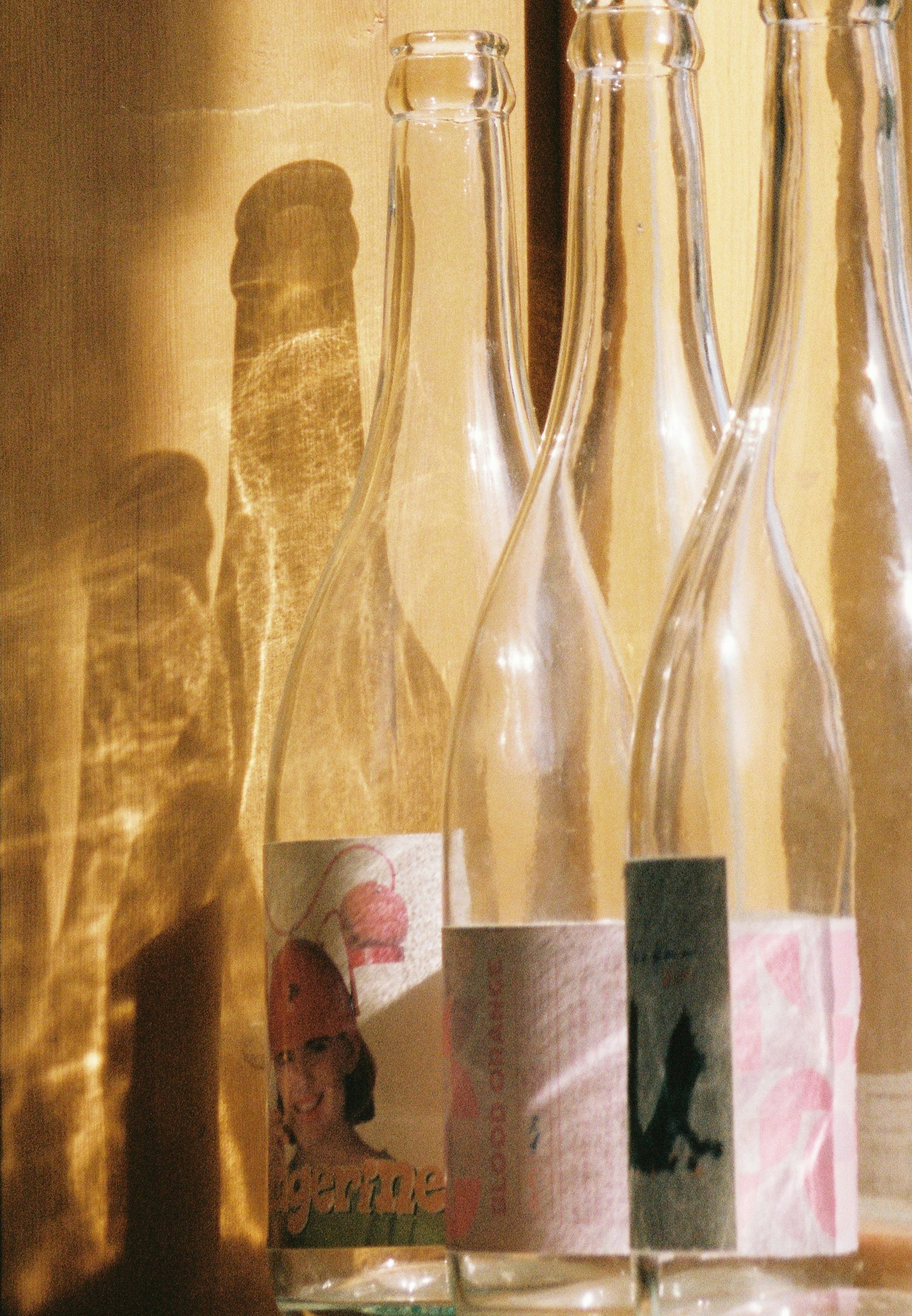 Several transparent bottles with labels casting shadows on a golden background