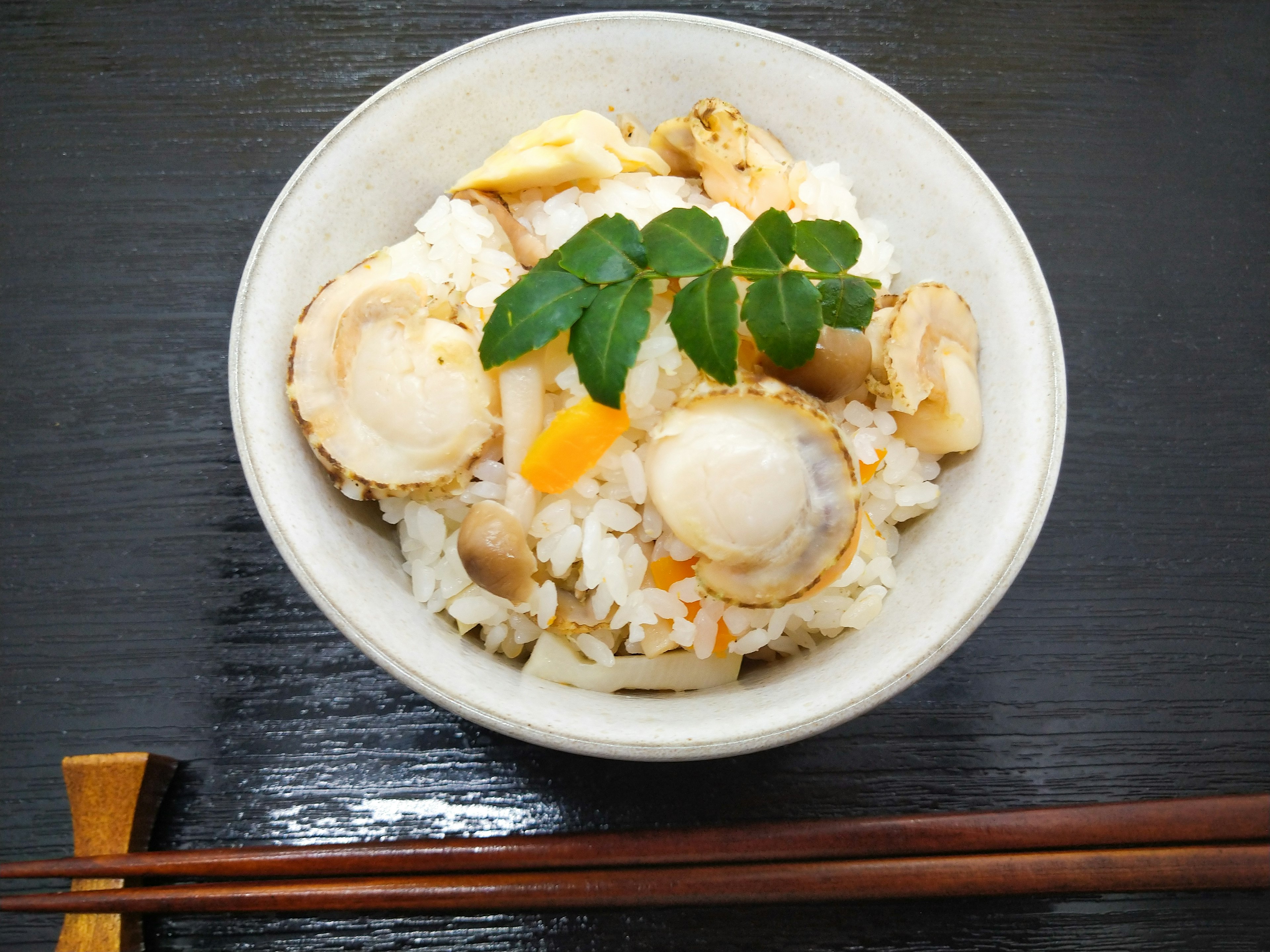 Bowl of rice topped with shellfish and vegetables garnished with green leaves