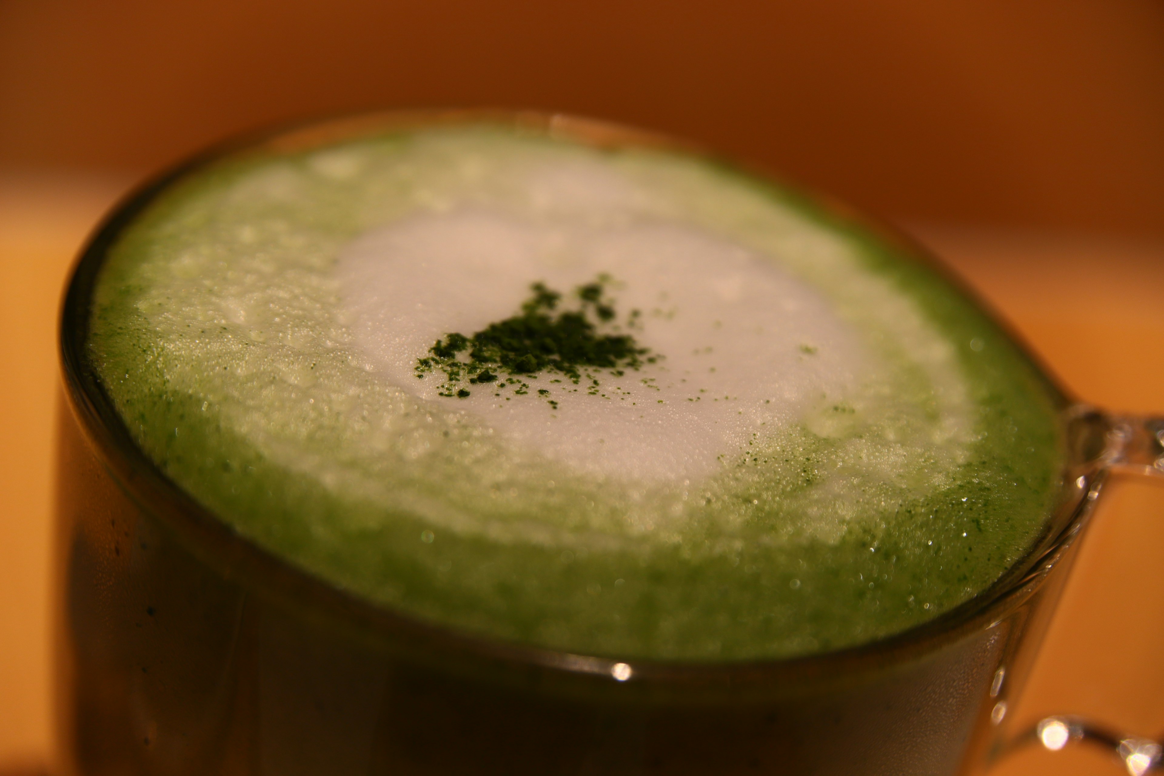 A frothy green beverage topped with white foam and green powder in a glass cup