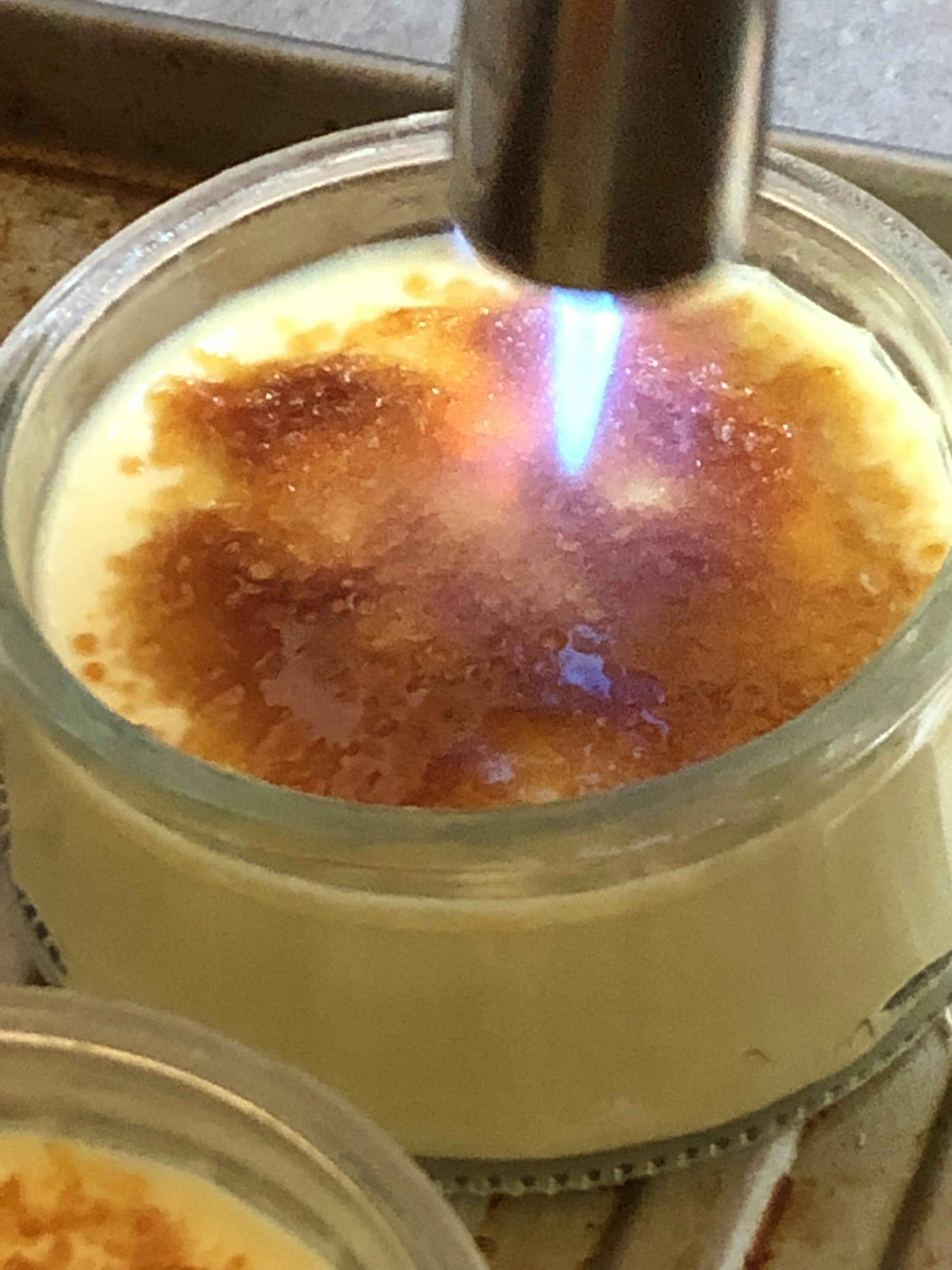 A kitchen torch caramelizing the top of a creamy dessert