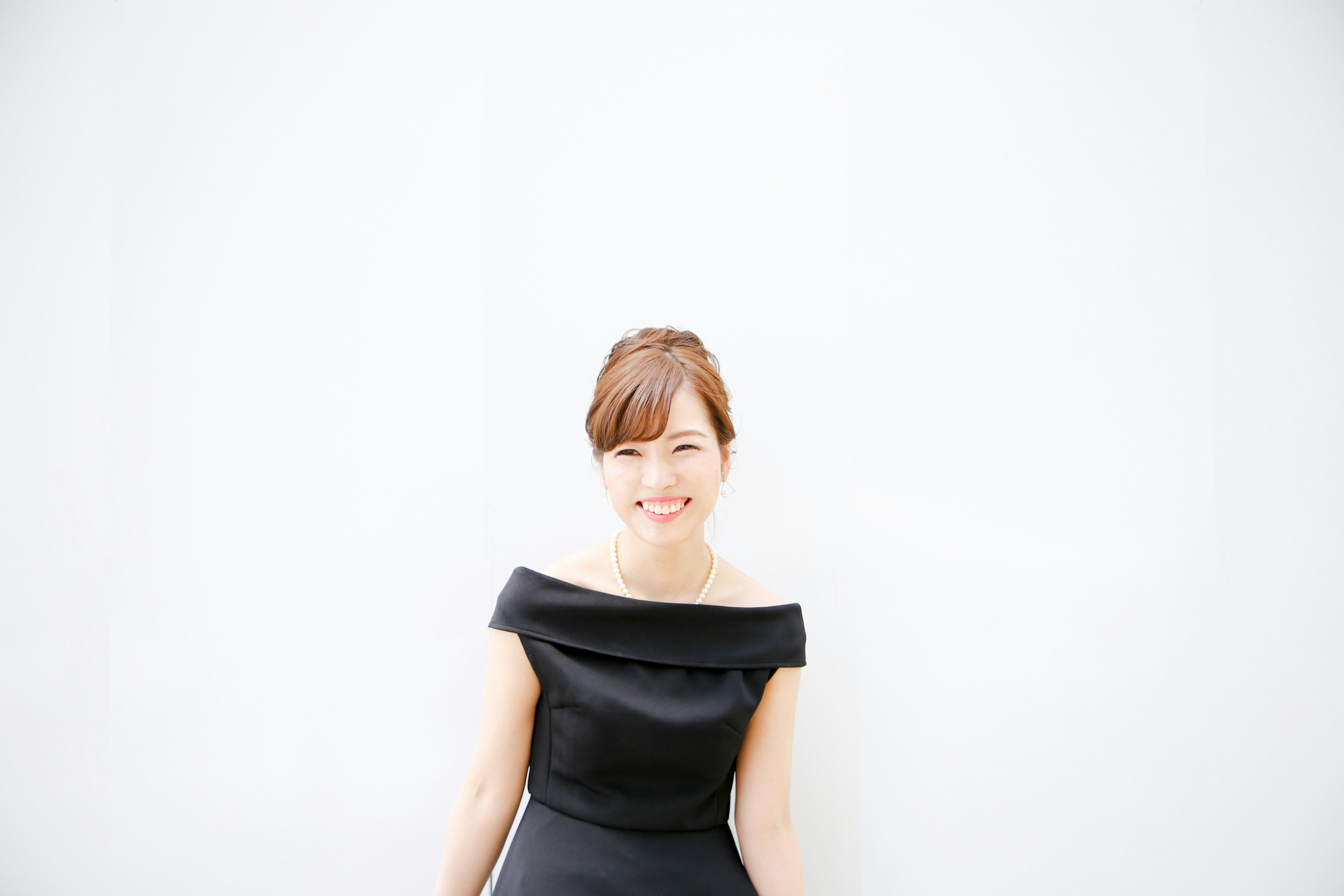 Retrato de una mujer sonriente con un vestido negro frente a un fondo blanco