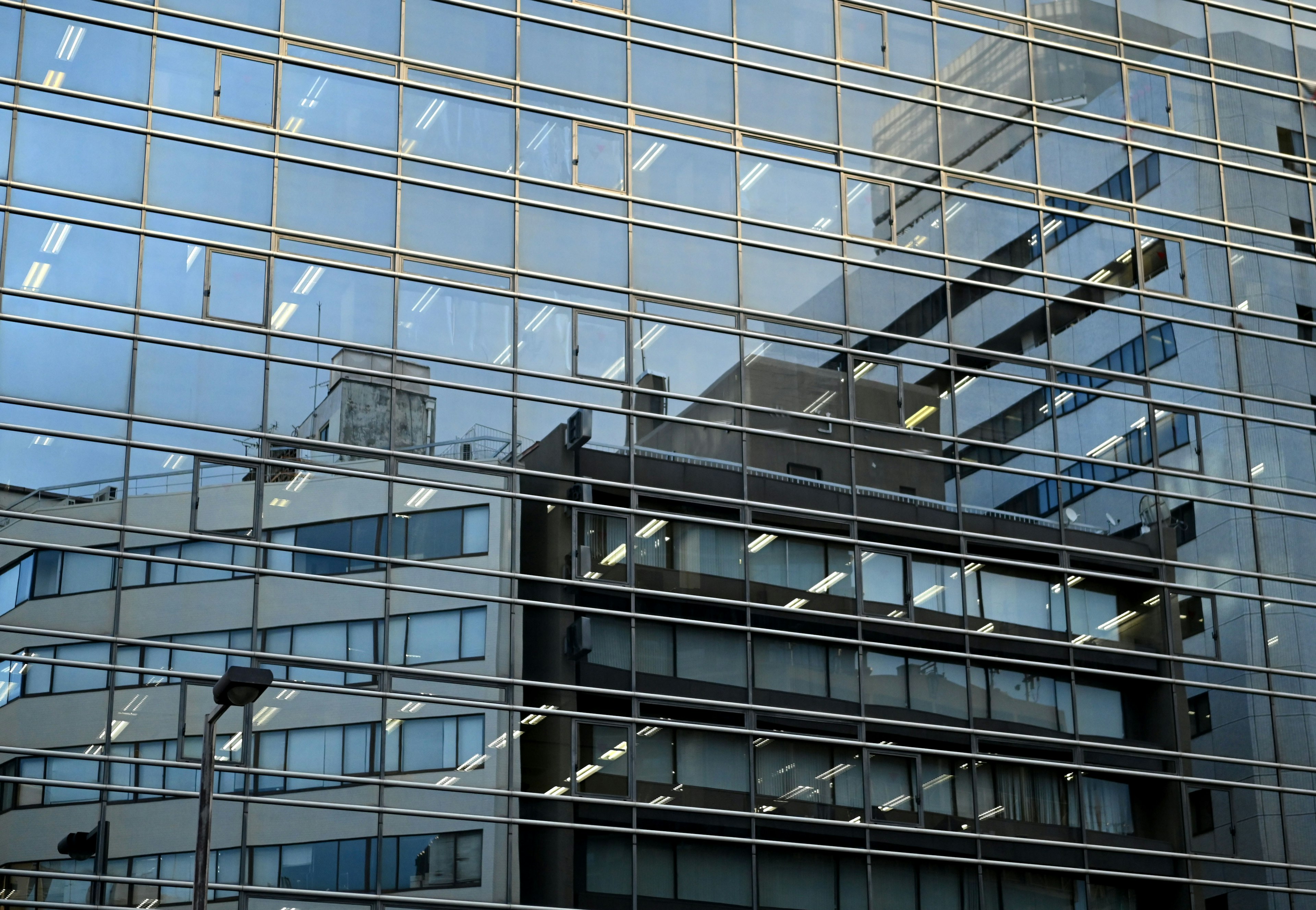 Fachada de vidrio de un edificio moderno reflejando estructuras circundantes y luces