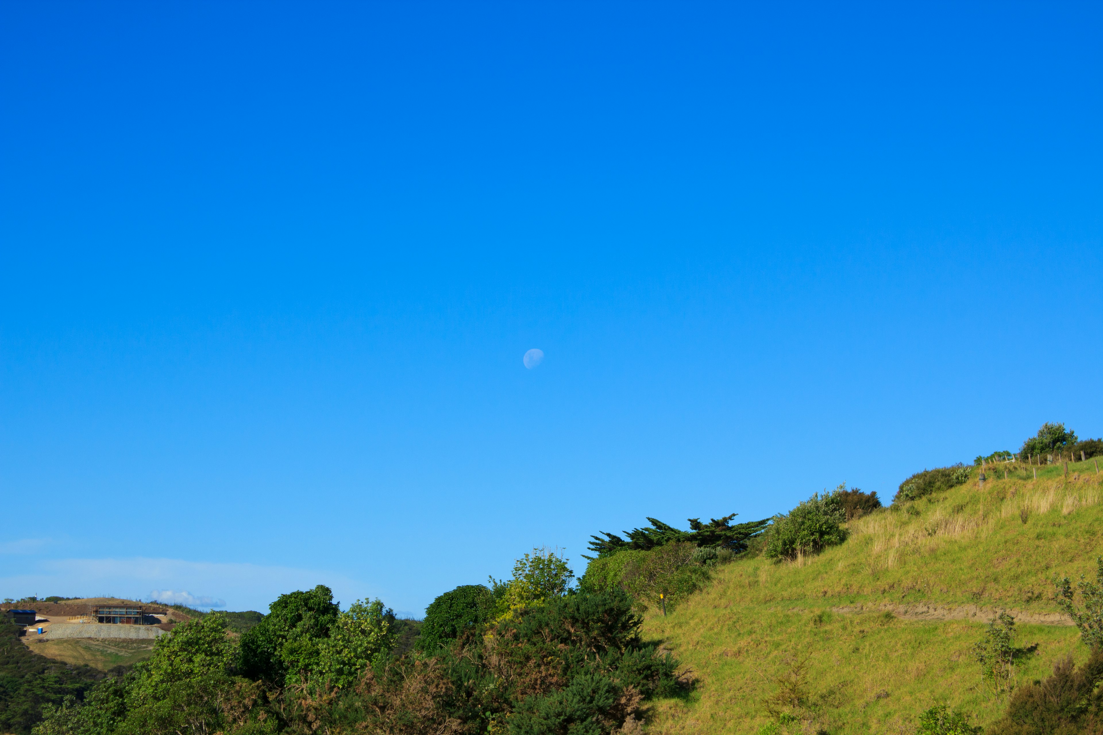 Luna en un cielo azul claro sobre colinas verdes