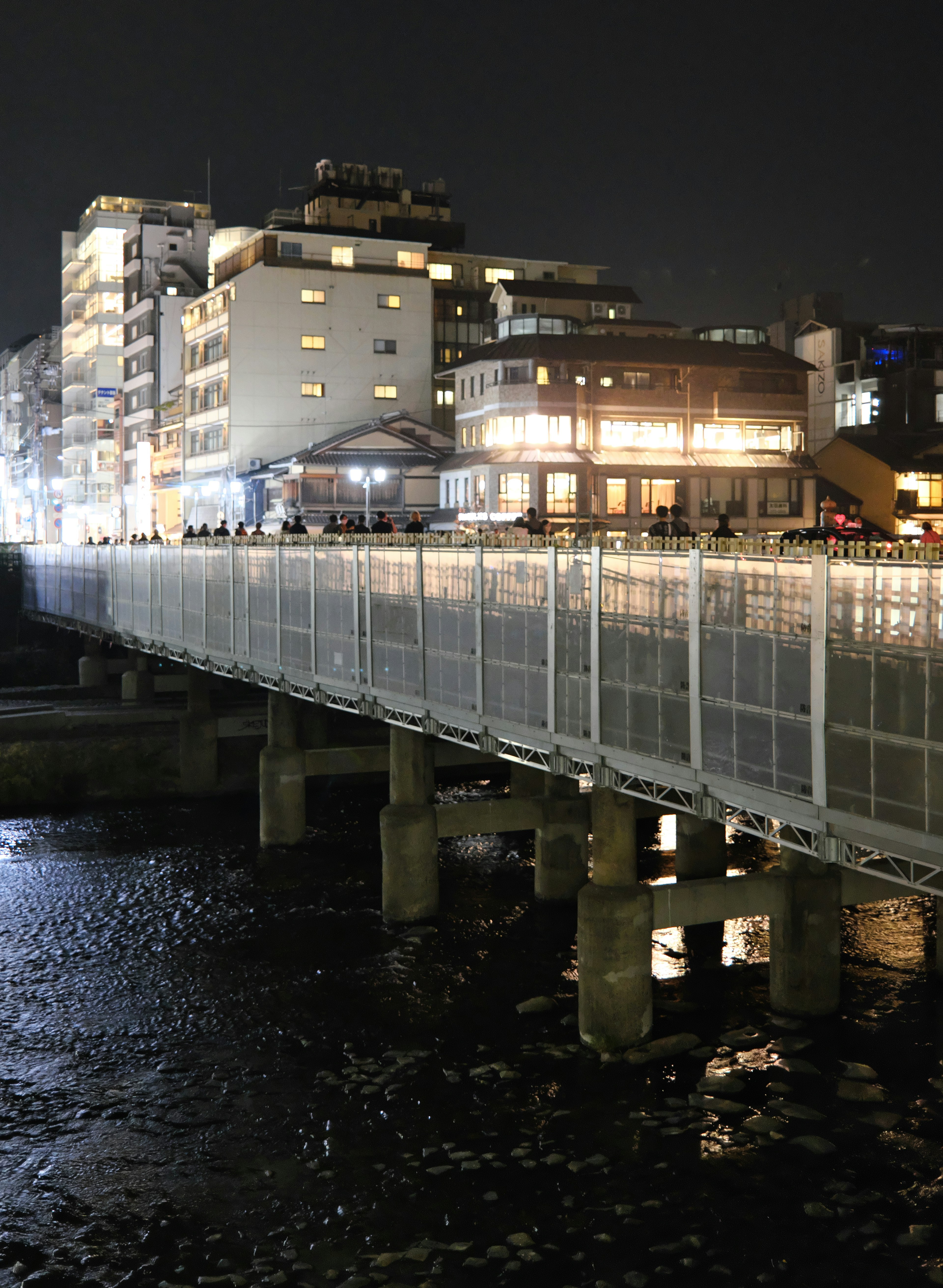 Vista nocturna de un puente peatonal con edificios iluminados