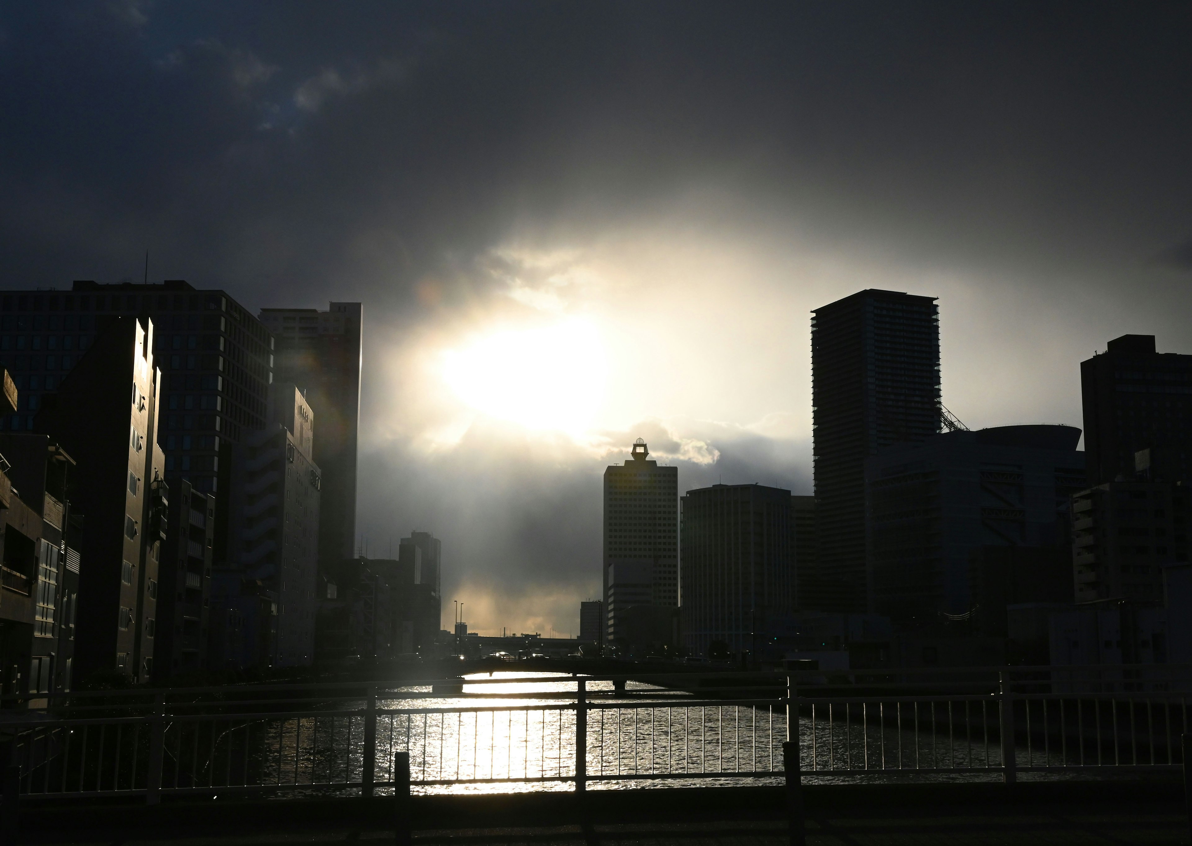 Silhouette of city buildings with a river under a setting sun