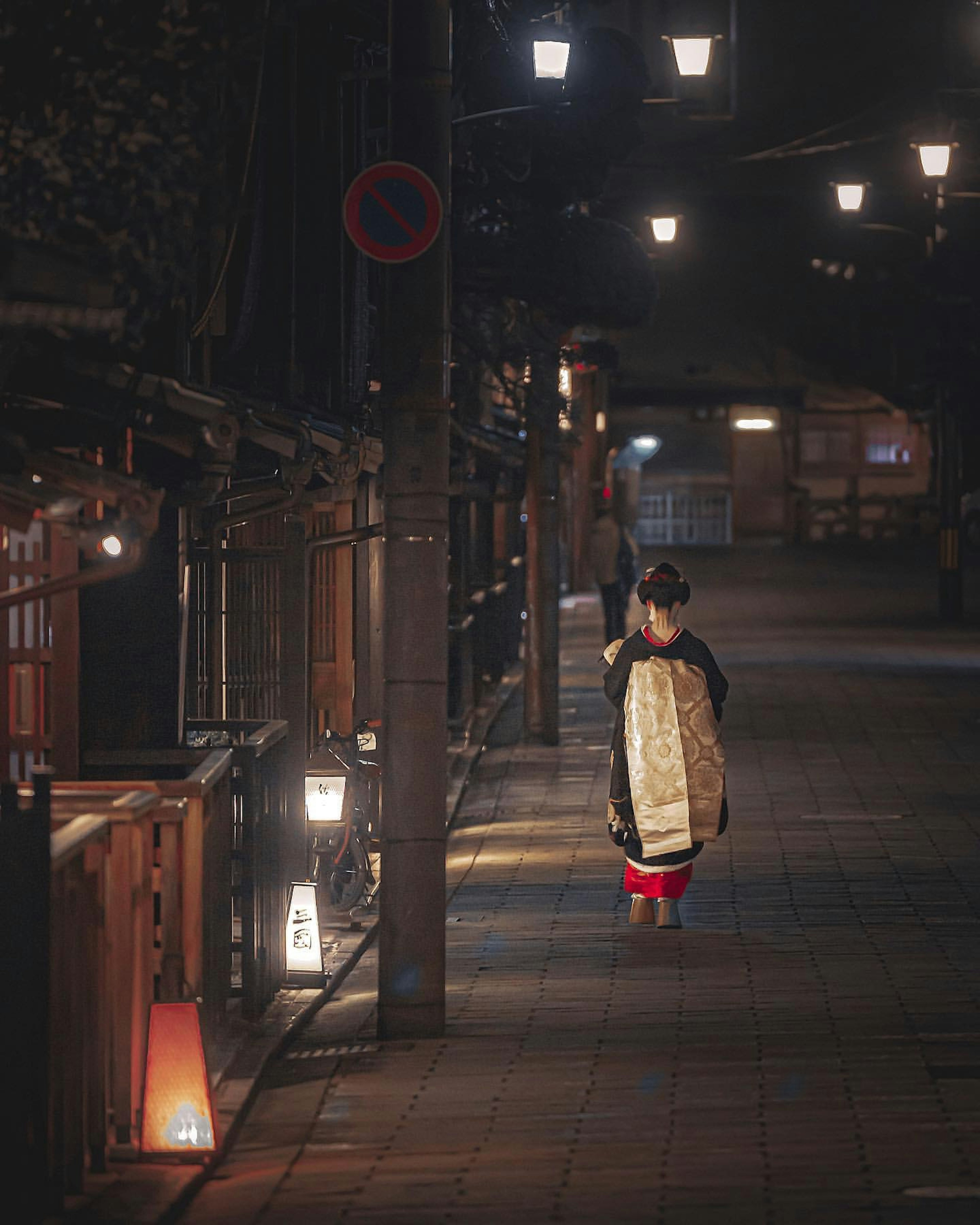 Woman in kimono walking down a lit street at night