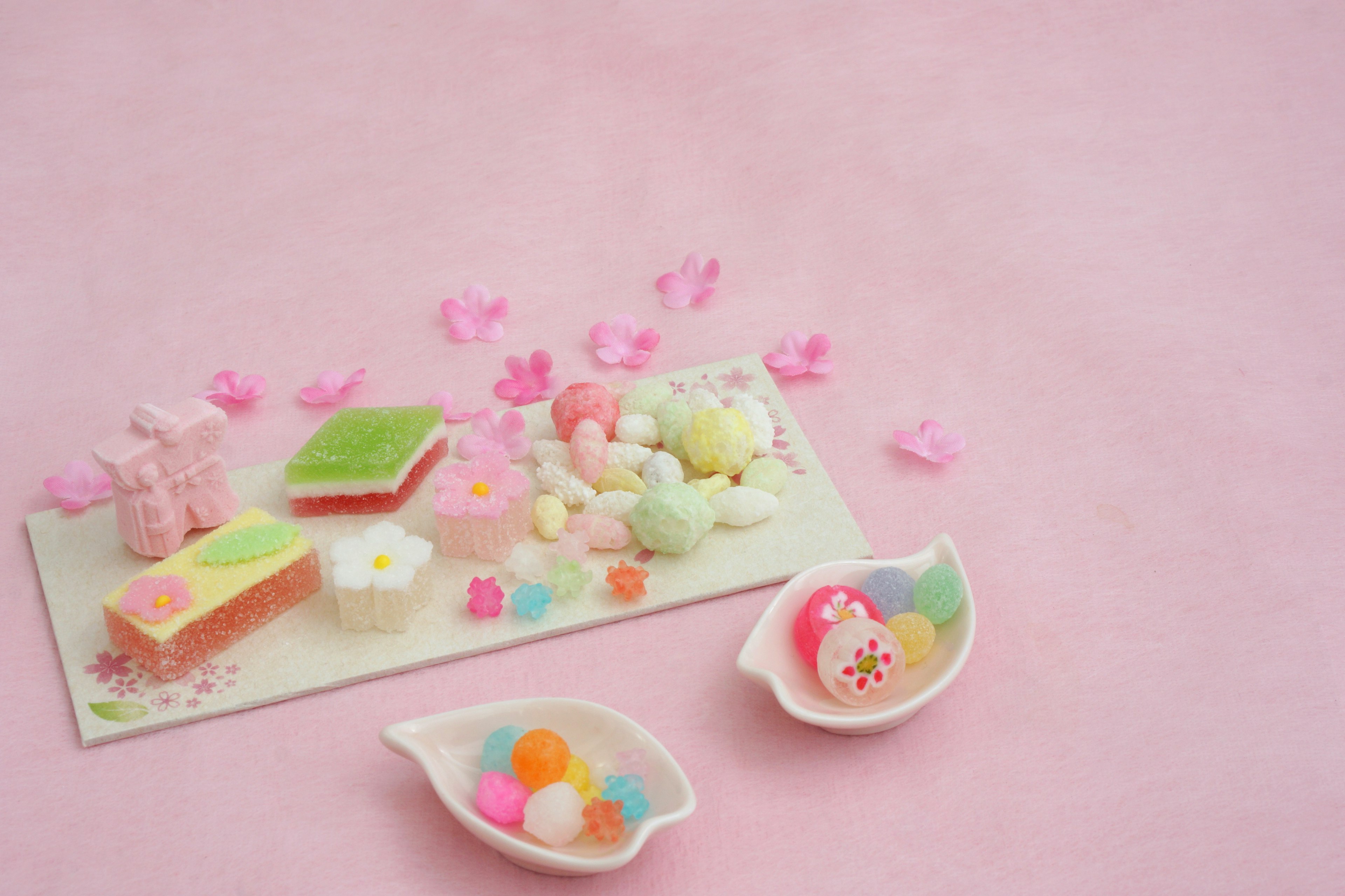 Colorful Japanese sweets arranged on a pale pink background with decorative flower petals