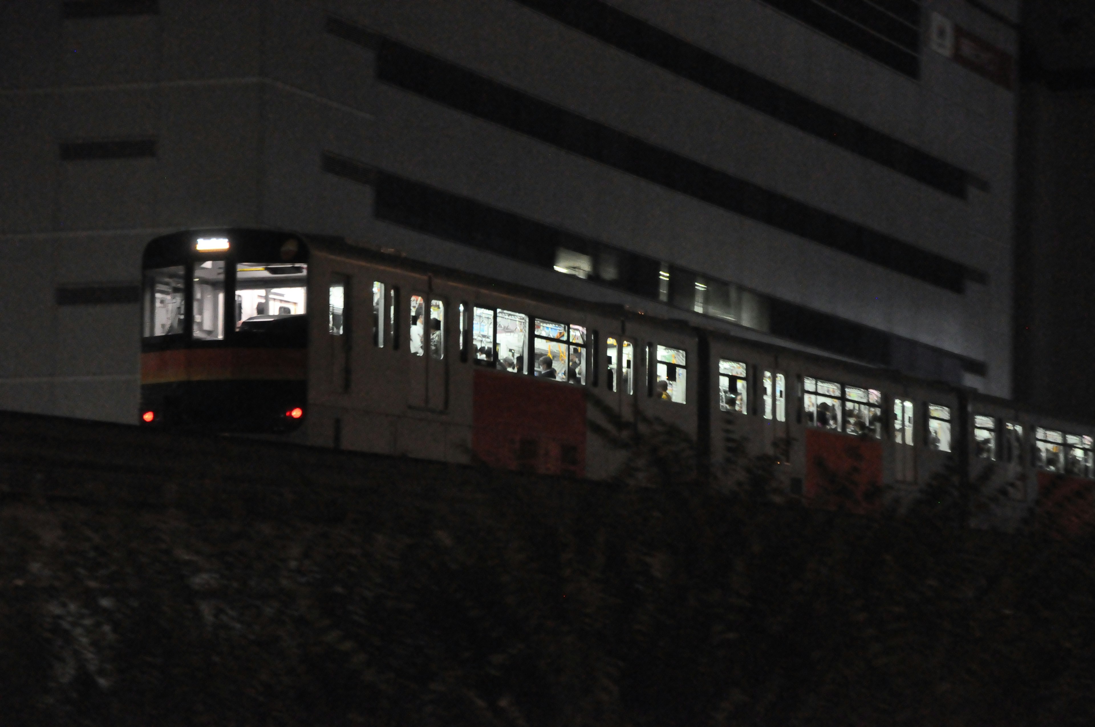 Tren iluminado por la noche pasando junto a un edificio