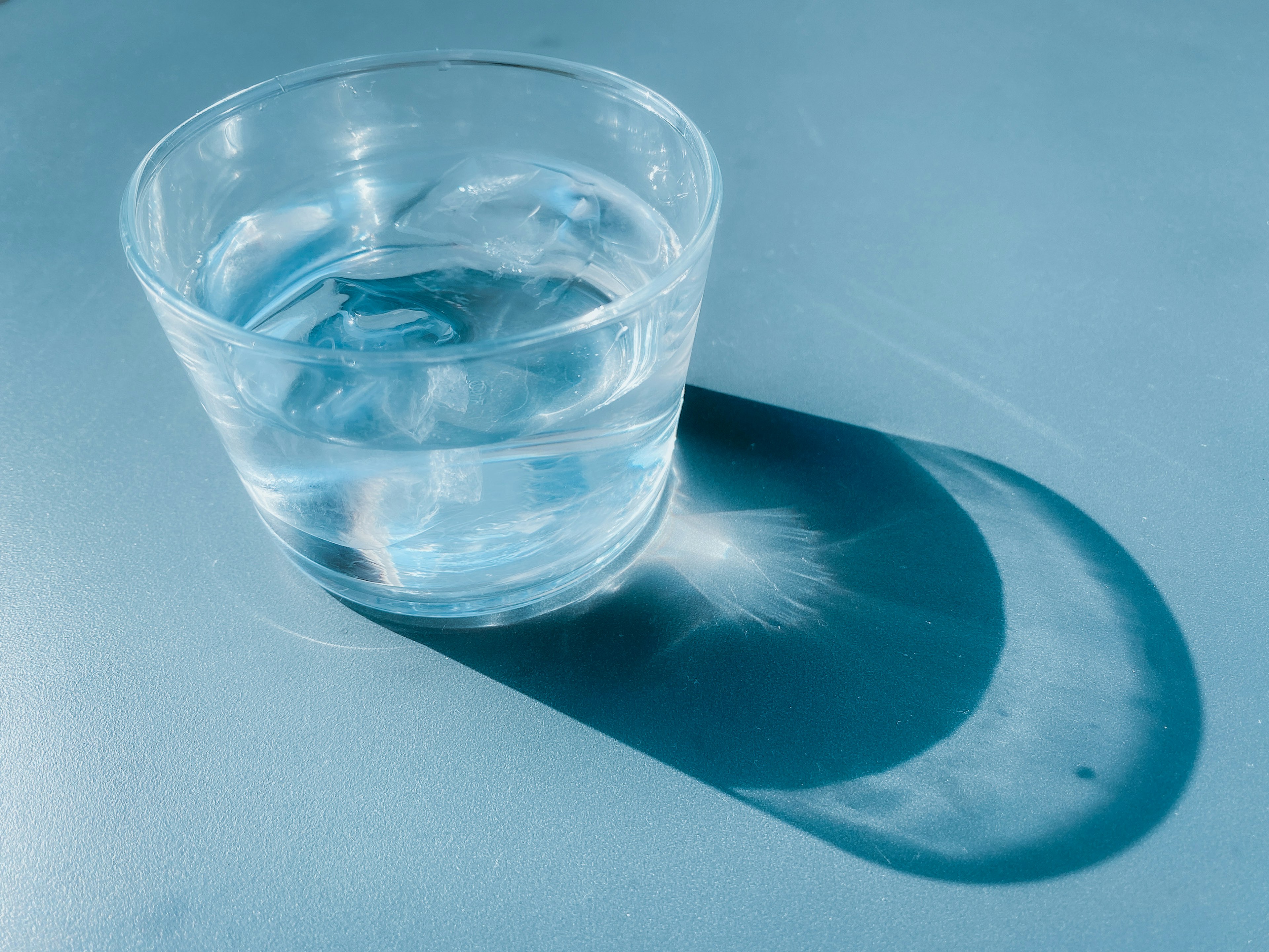 Ein klares Glas mit Eiswasser, das einen sanften Schatten auf eine blaue Oberfläche wirft