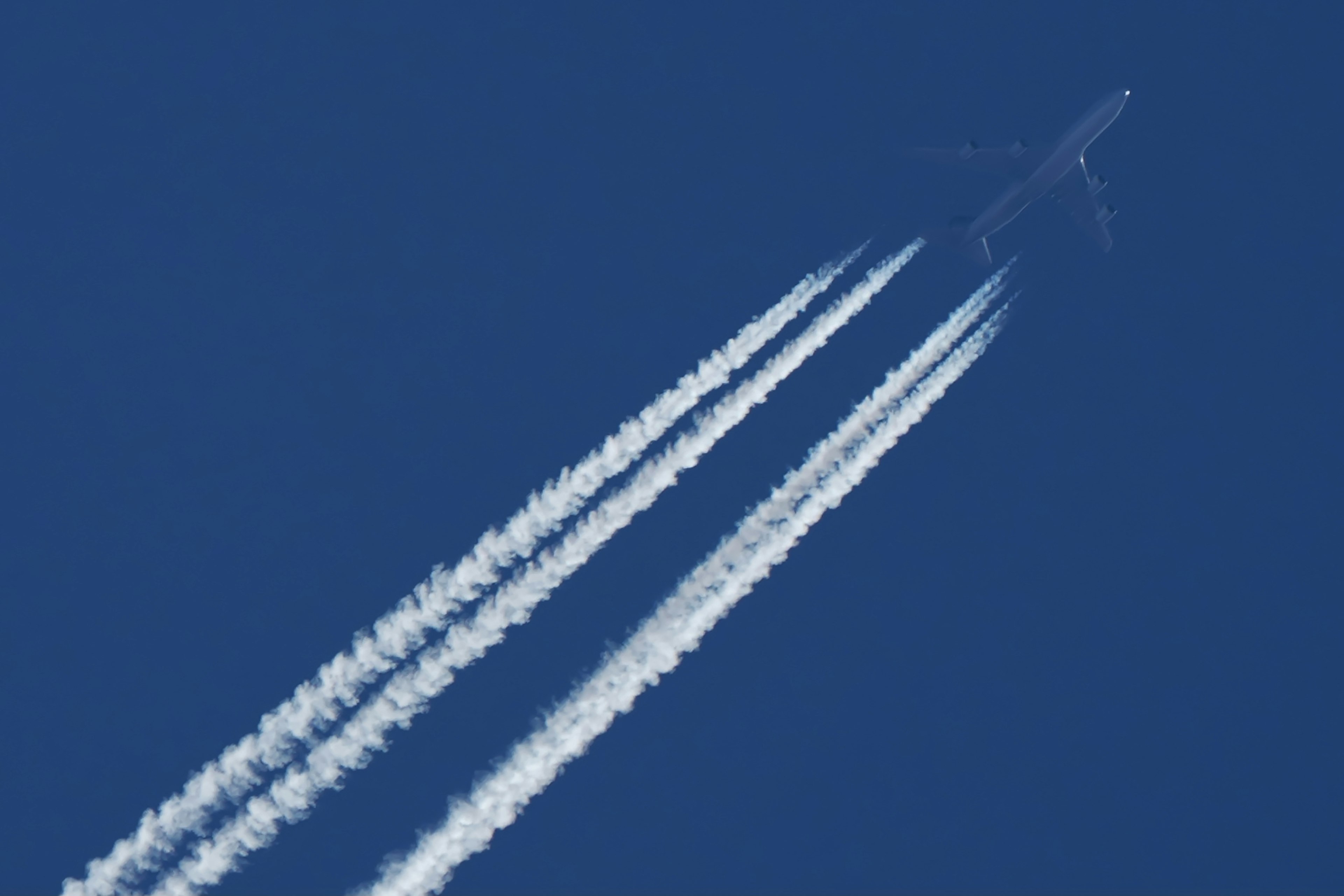 Un avión volando en un cielo azul dejando estelas blancas detrás