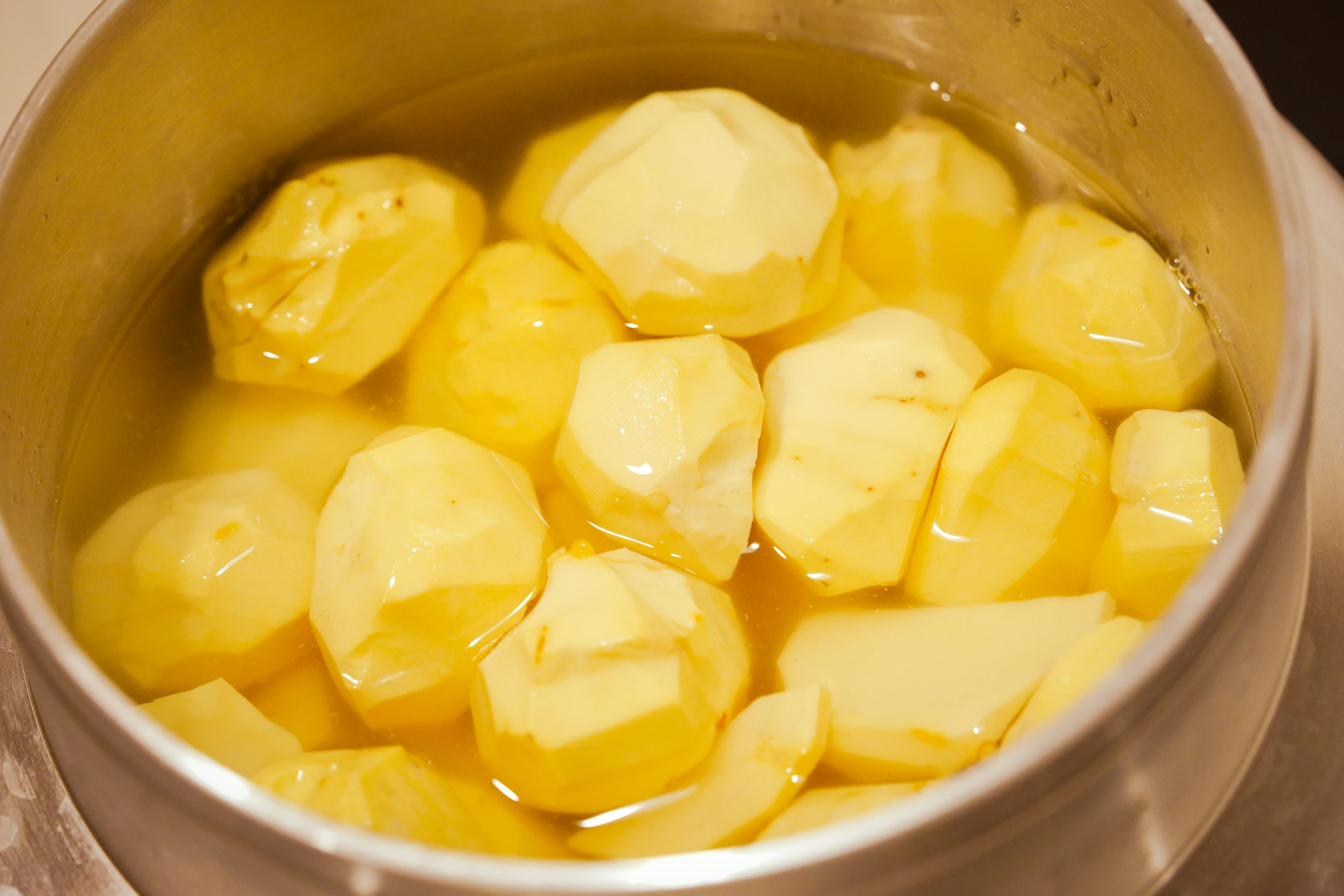 Peeled potatoes submerged in water in a pot