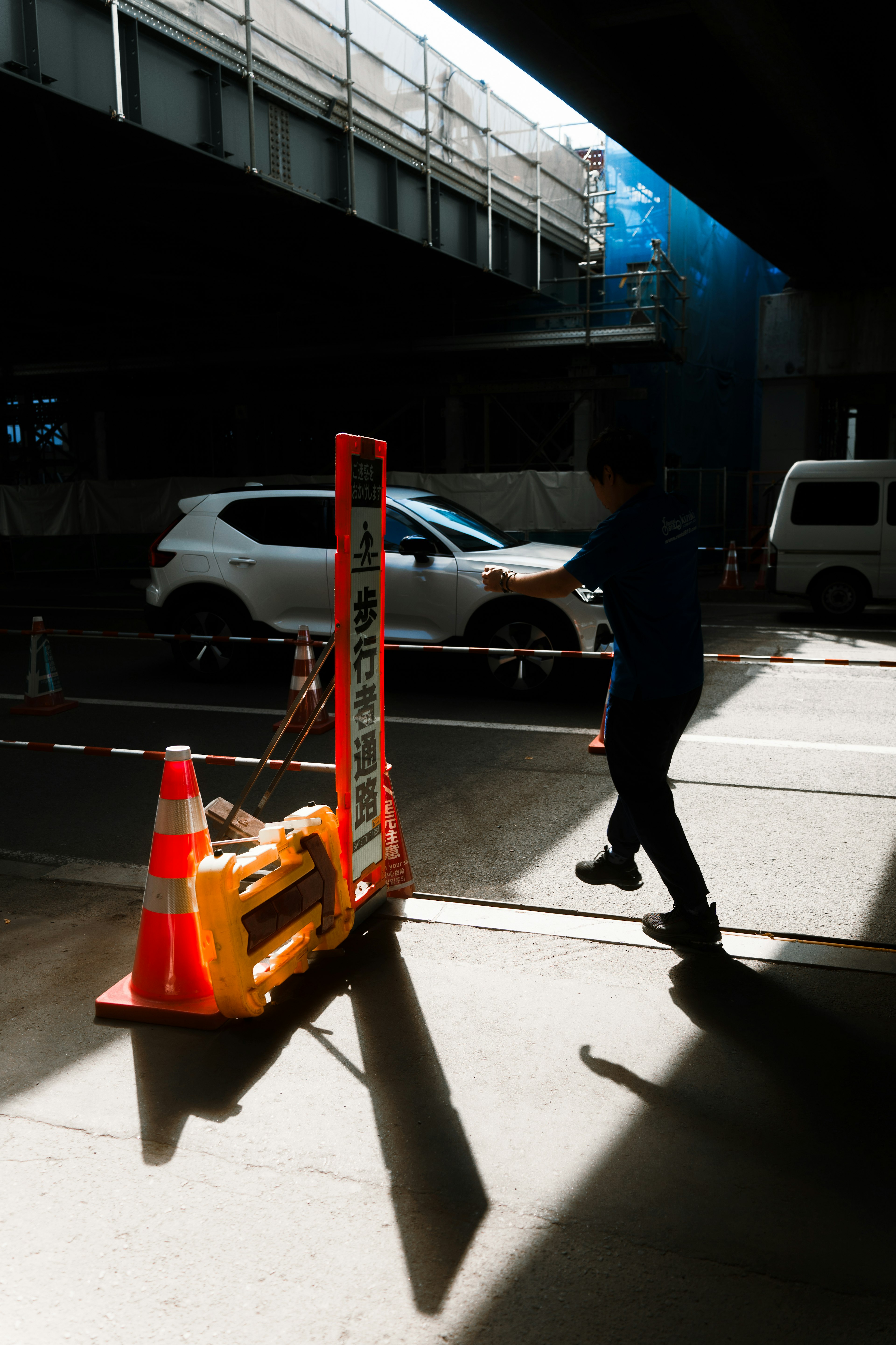 Escena urbana con un trabajador de construcción caminando junto a conos de tráfico