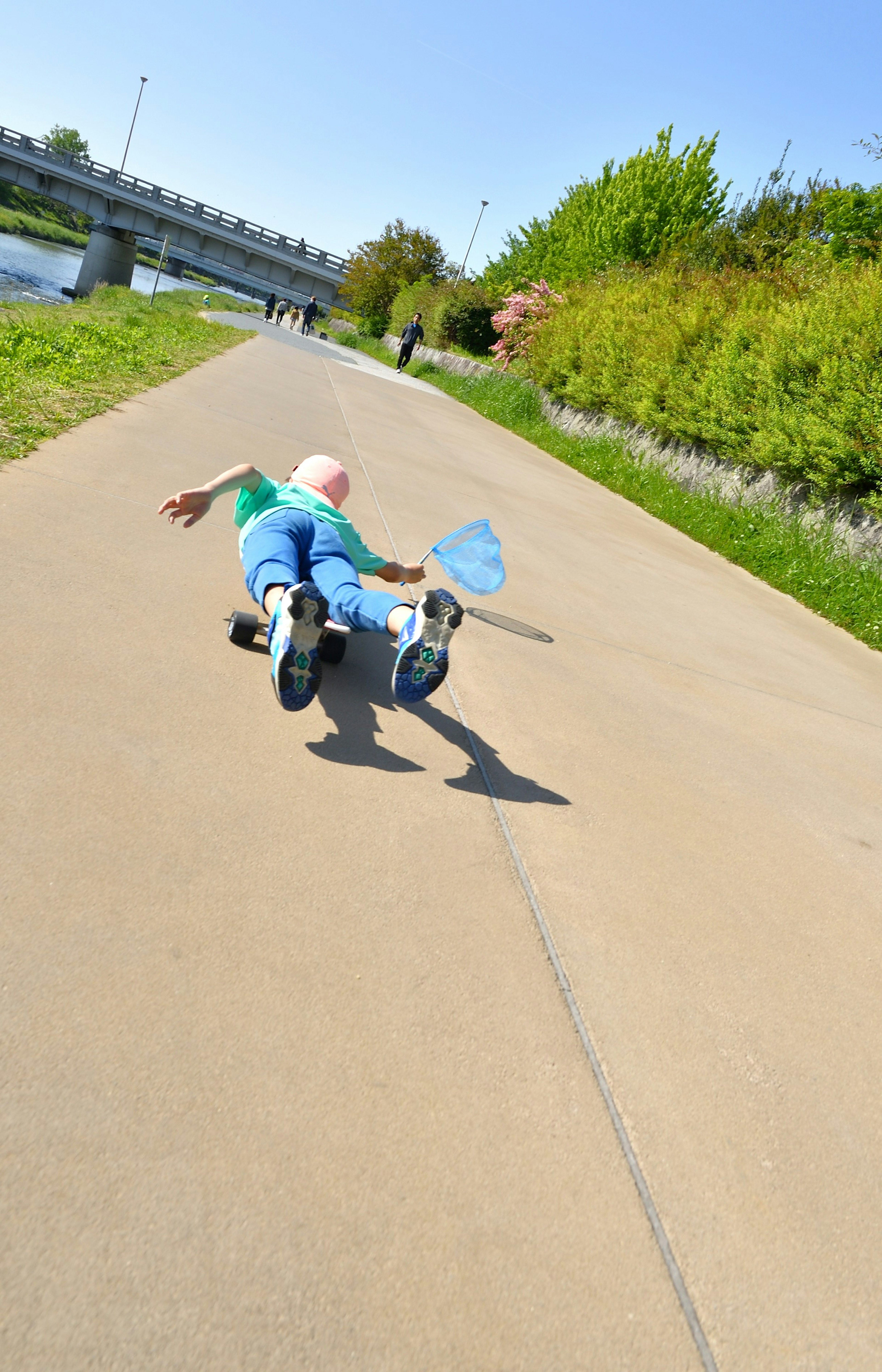 Child falling on a park pathway holding a blue bucket