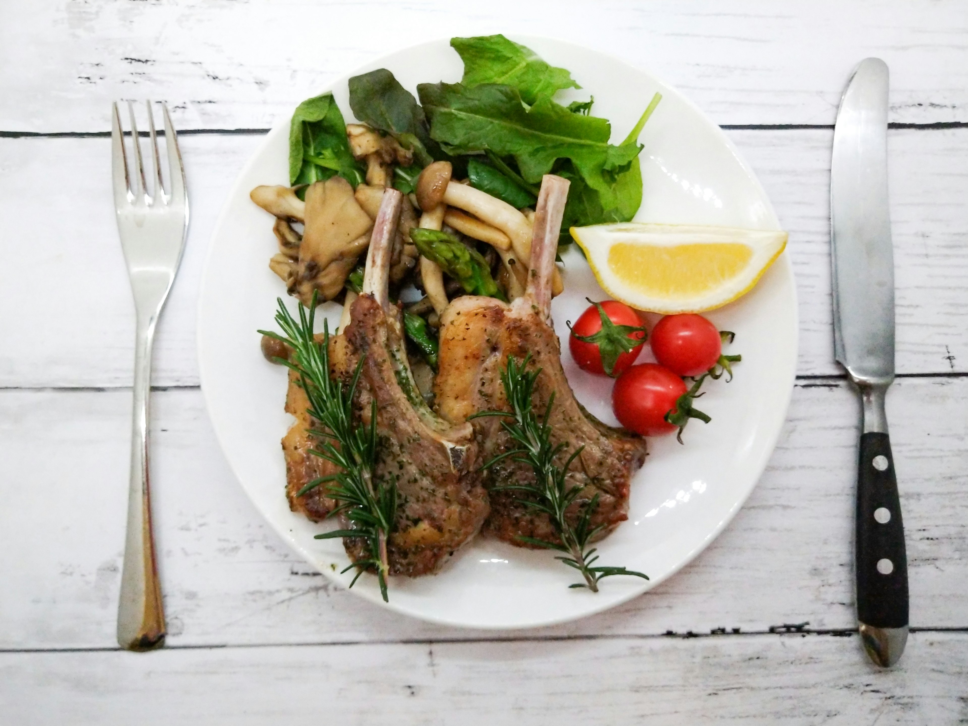 Lamb chops served on a white plate with salad and cherry tomatoes