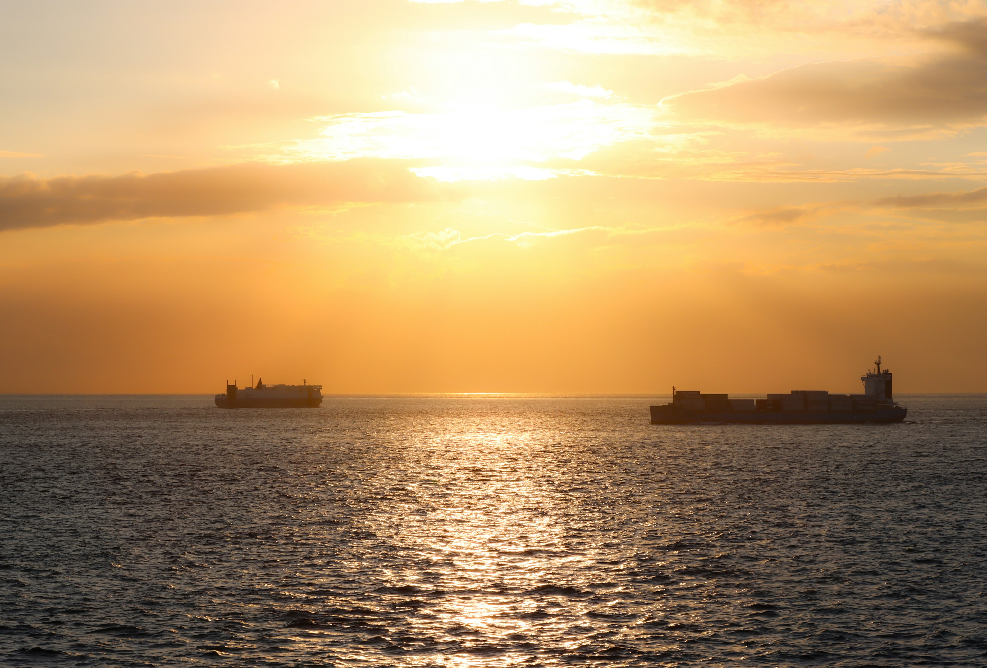 Zwei Schiffe auf dem Ozean mit einem Sonnenuntergang, der sich im Wasser spiegelt