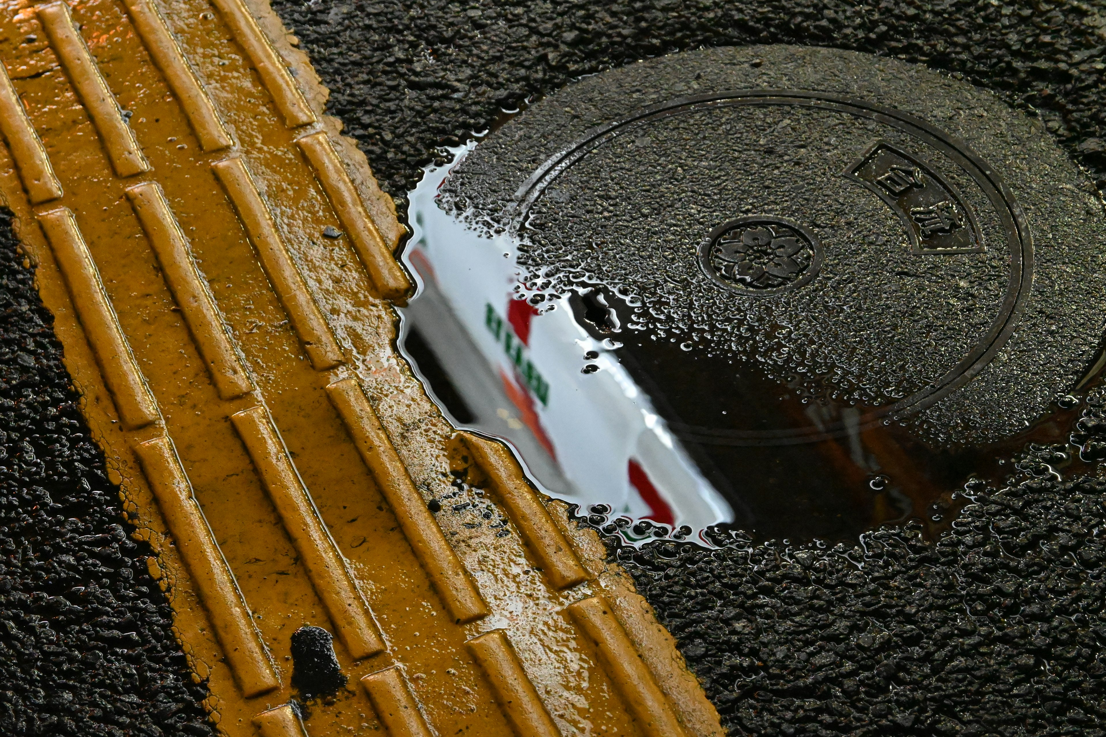 Riflesso di un tombino in una pozzanghera sulla strada