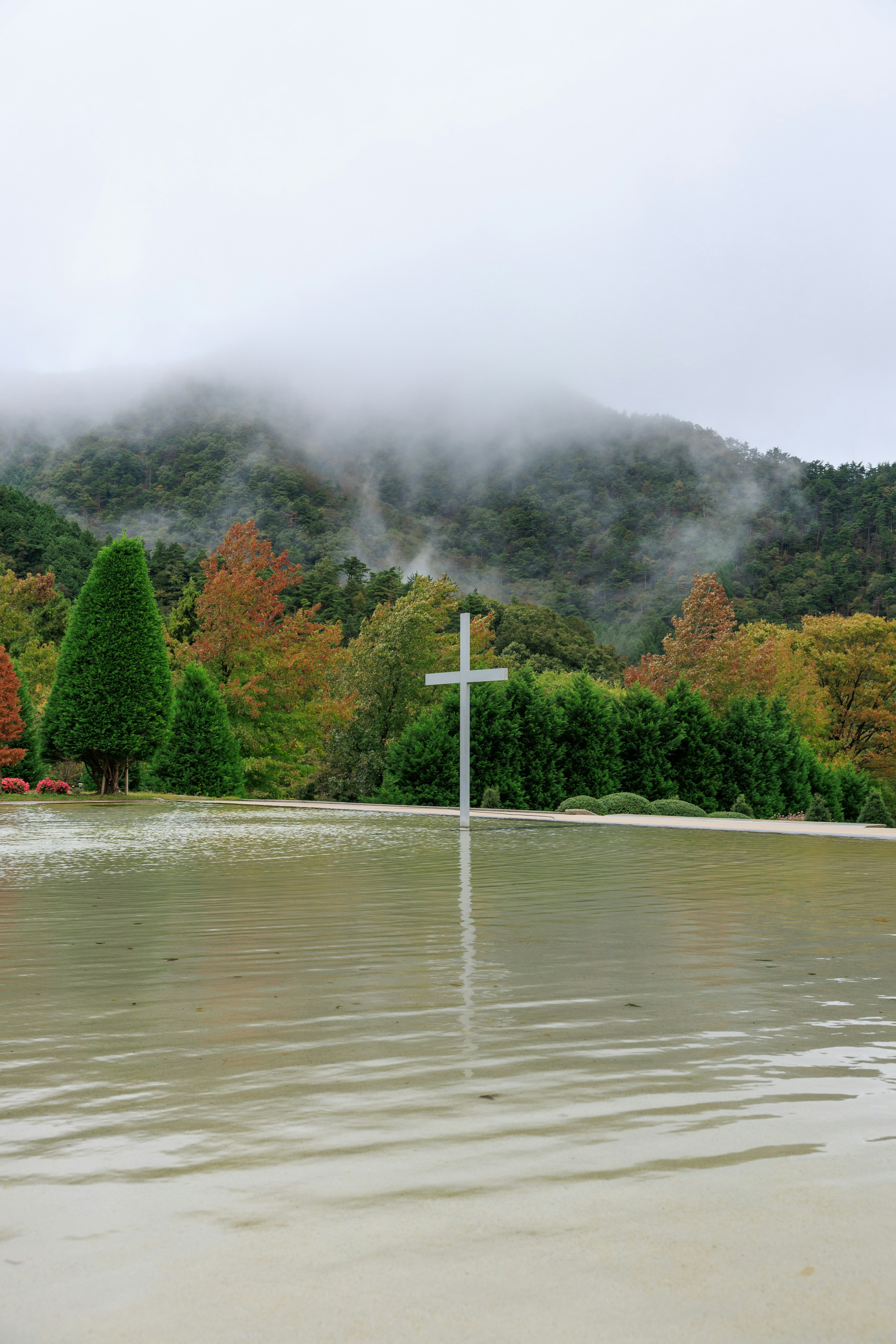 霧がかかった山と水に浸かった十字架が映る風景