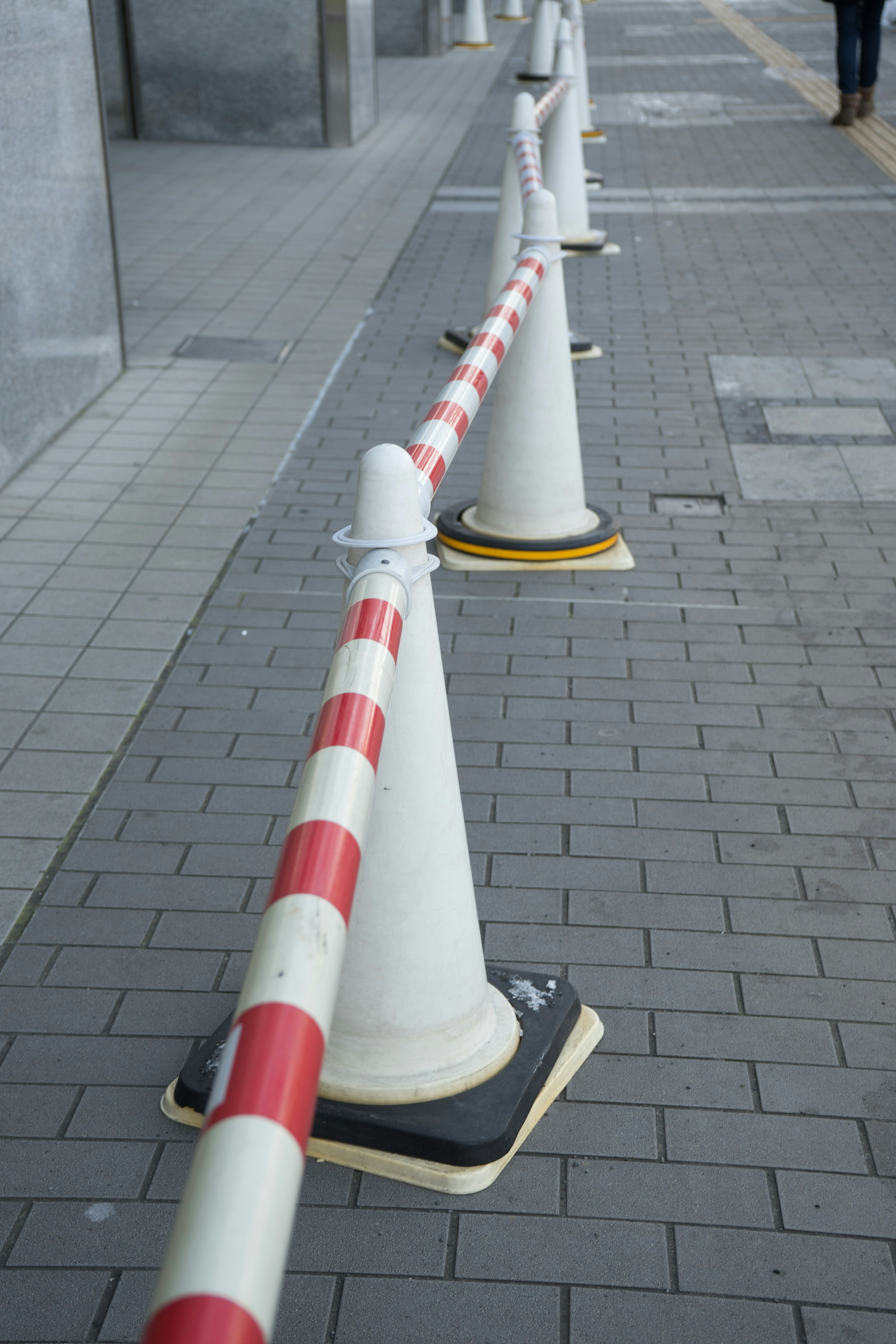 A row of traffic cones with red and white striped barrier tape on a sidewalk