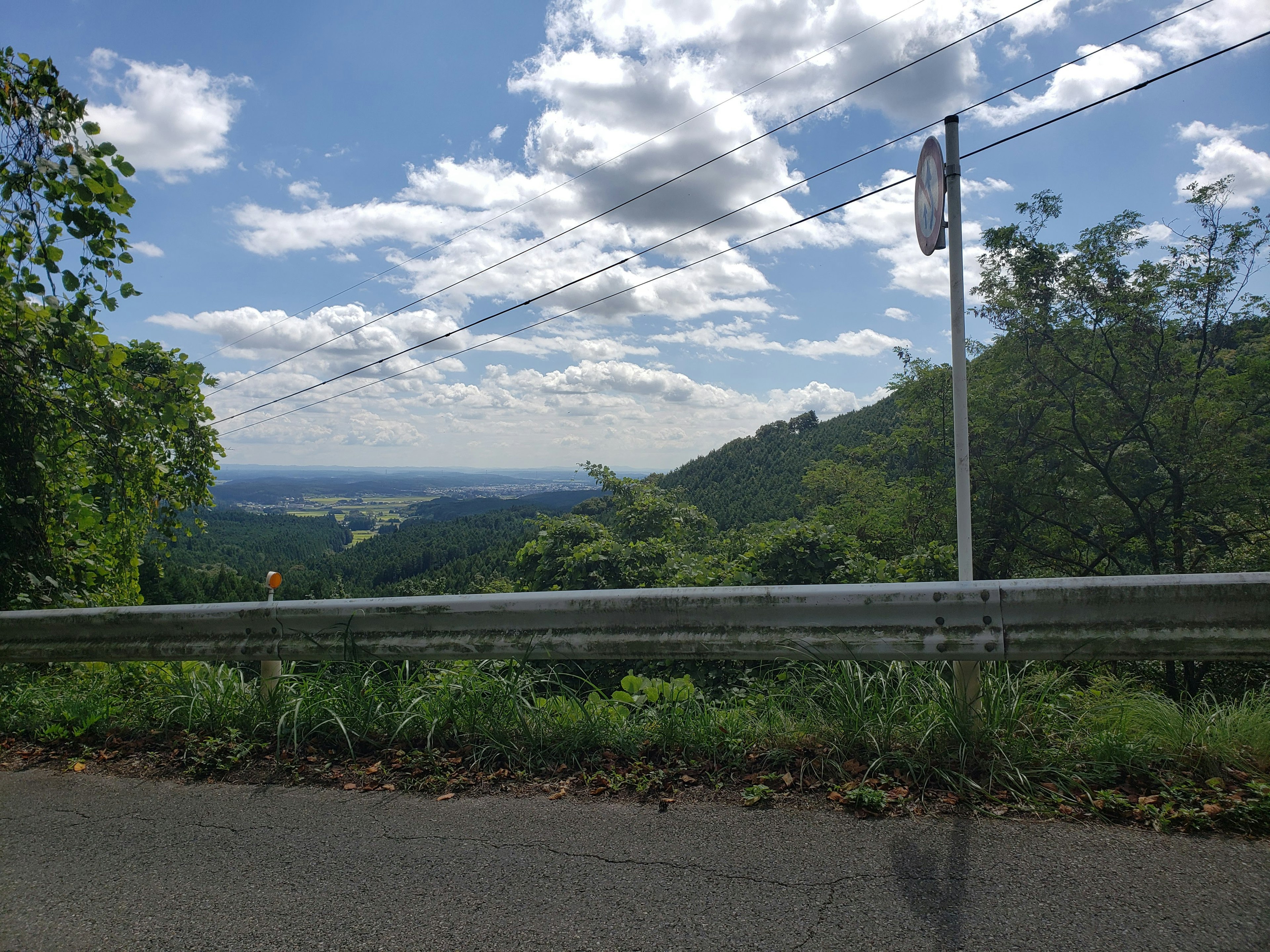 Scenic view with blue sky and white clouds lush green mountains and a roadside barrier