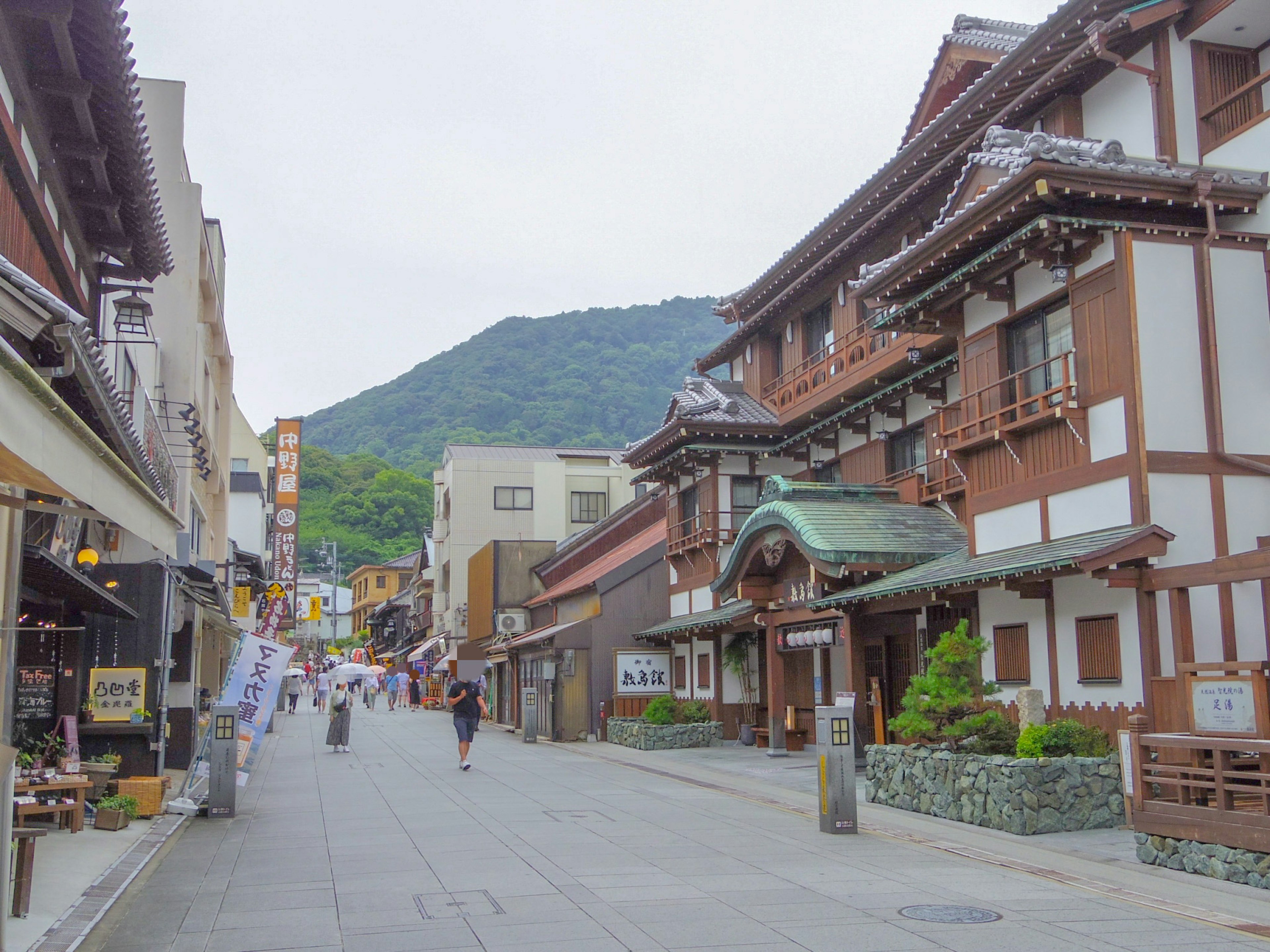 Vista escénica de una ciudad termal con personas caminando y edificios japoneses tradicionales con una montaña de fondo