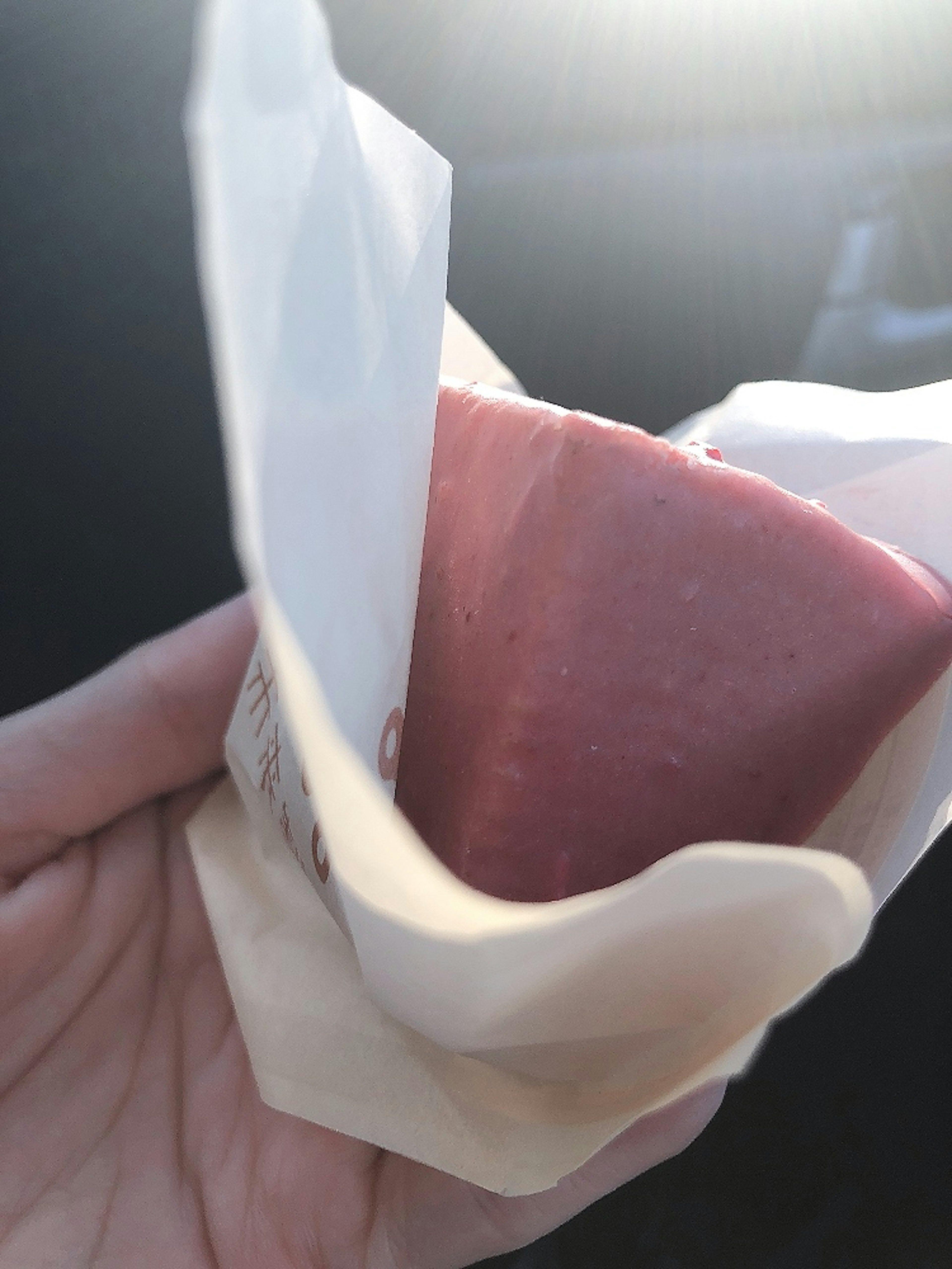 Ein pinkes Dessert, das wie Eiscreme aussieht, in einer Hand gehalten und in weißem Papier verpackt