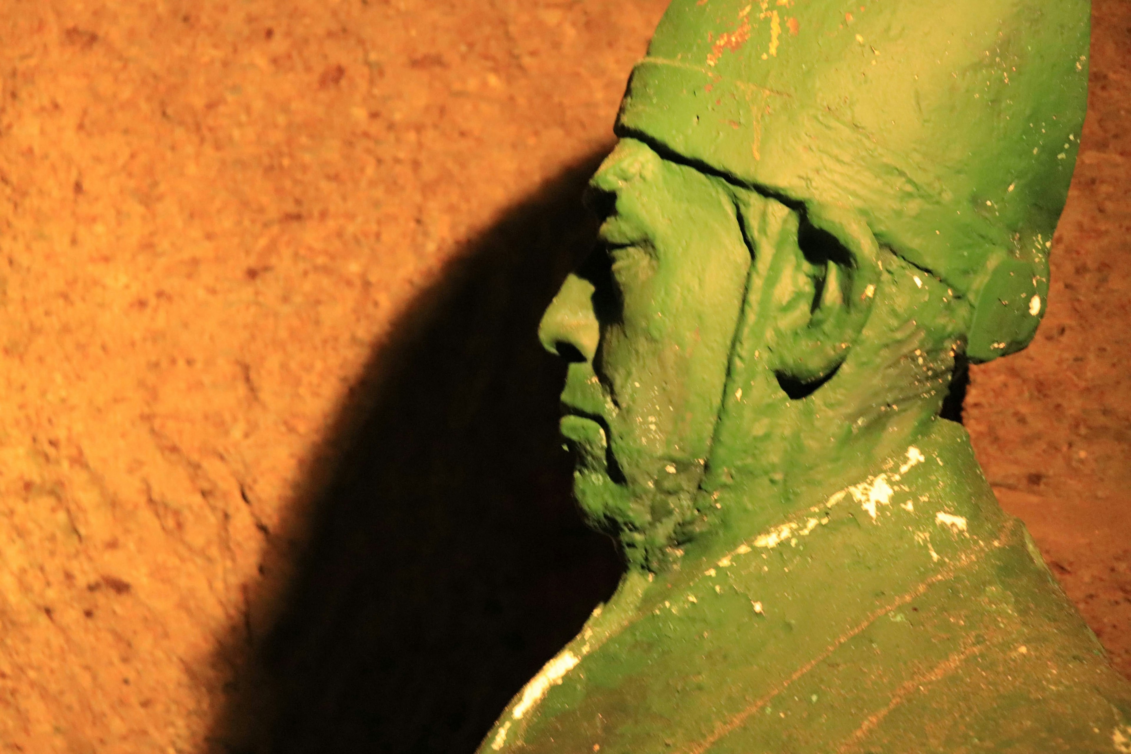 Profile view of a green statue against a dark background