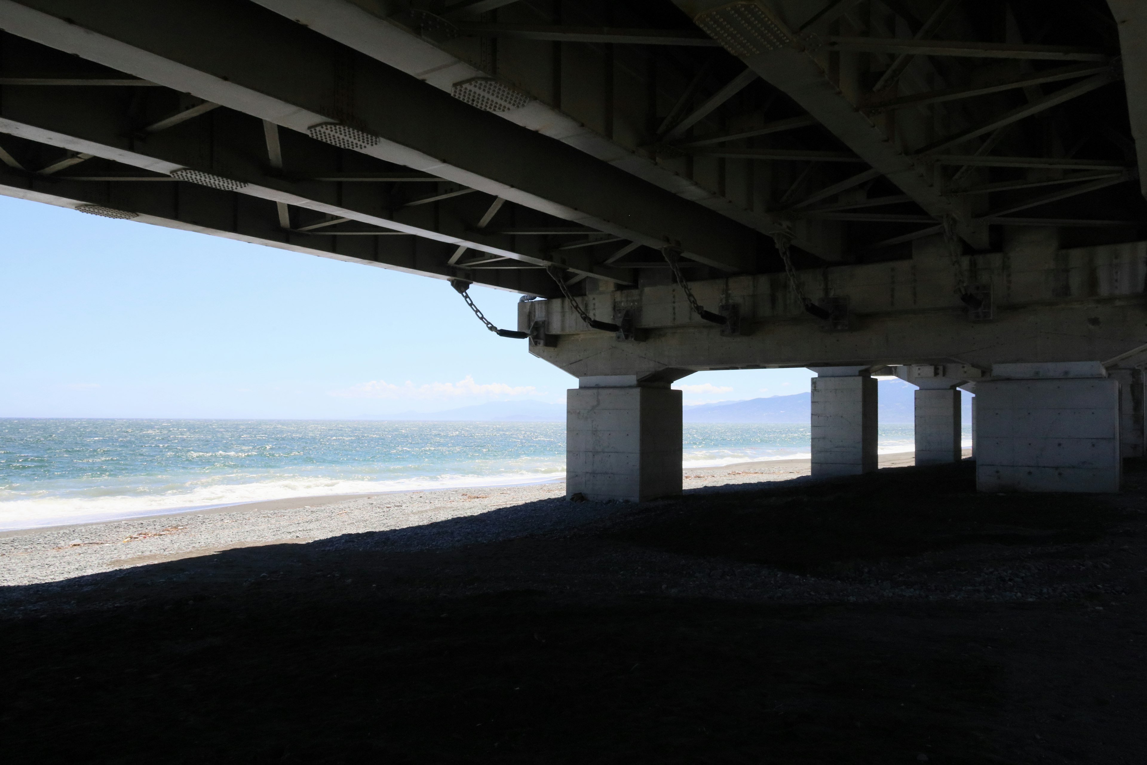 海岸の下にある橋の構造物の写真で青い空と波が見える