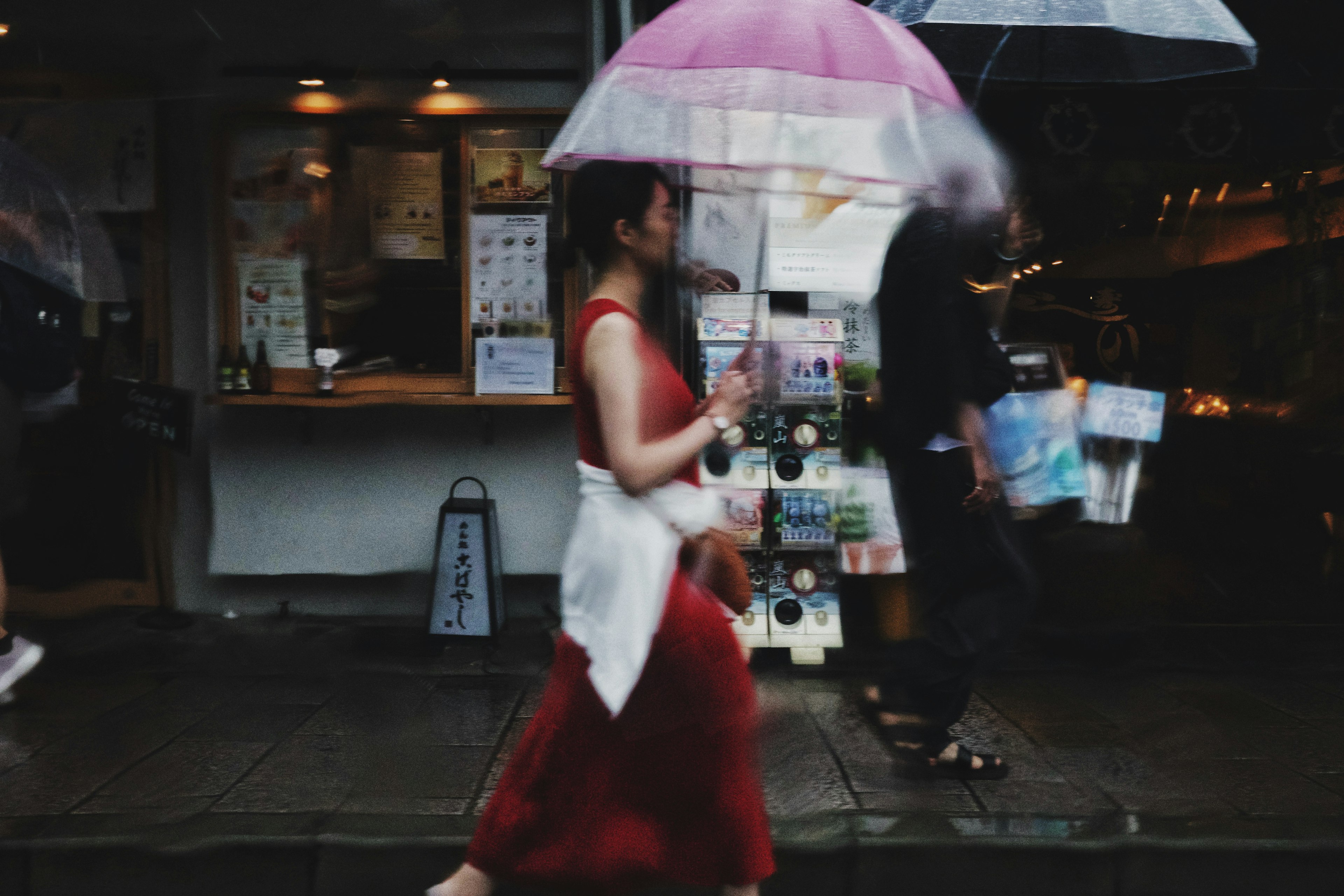 A woman in a red dress walking with a pink umbrella in a city street