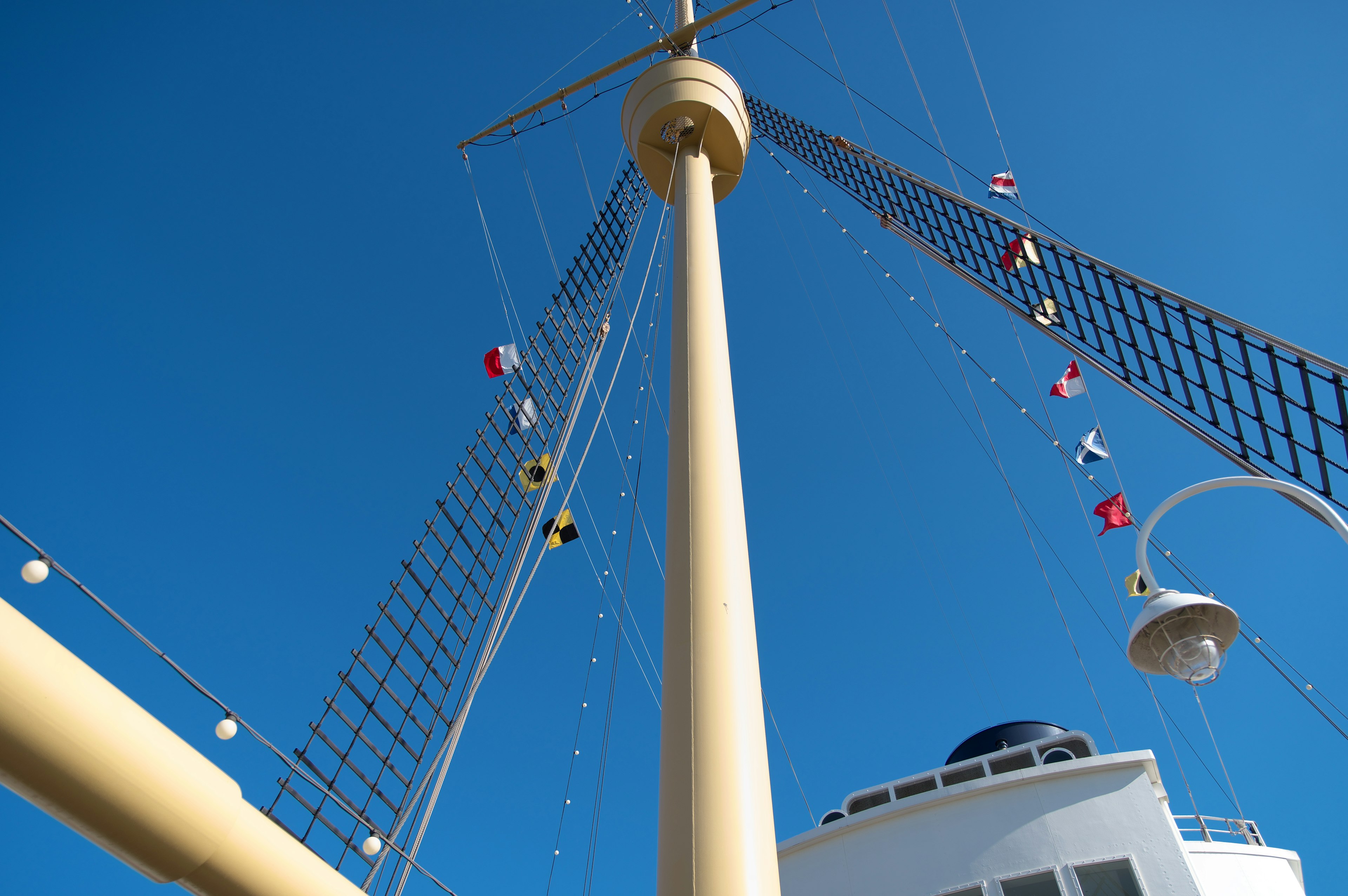 Schiffsmast mit bunten Fahnen vor klarem blauen Himmel