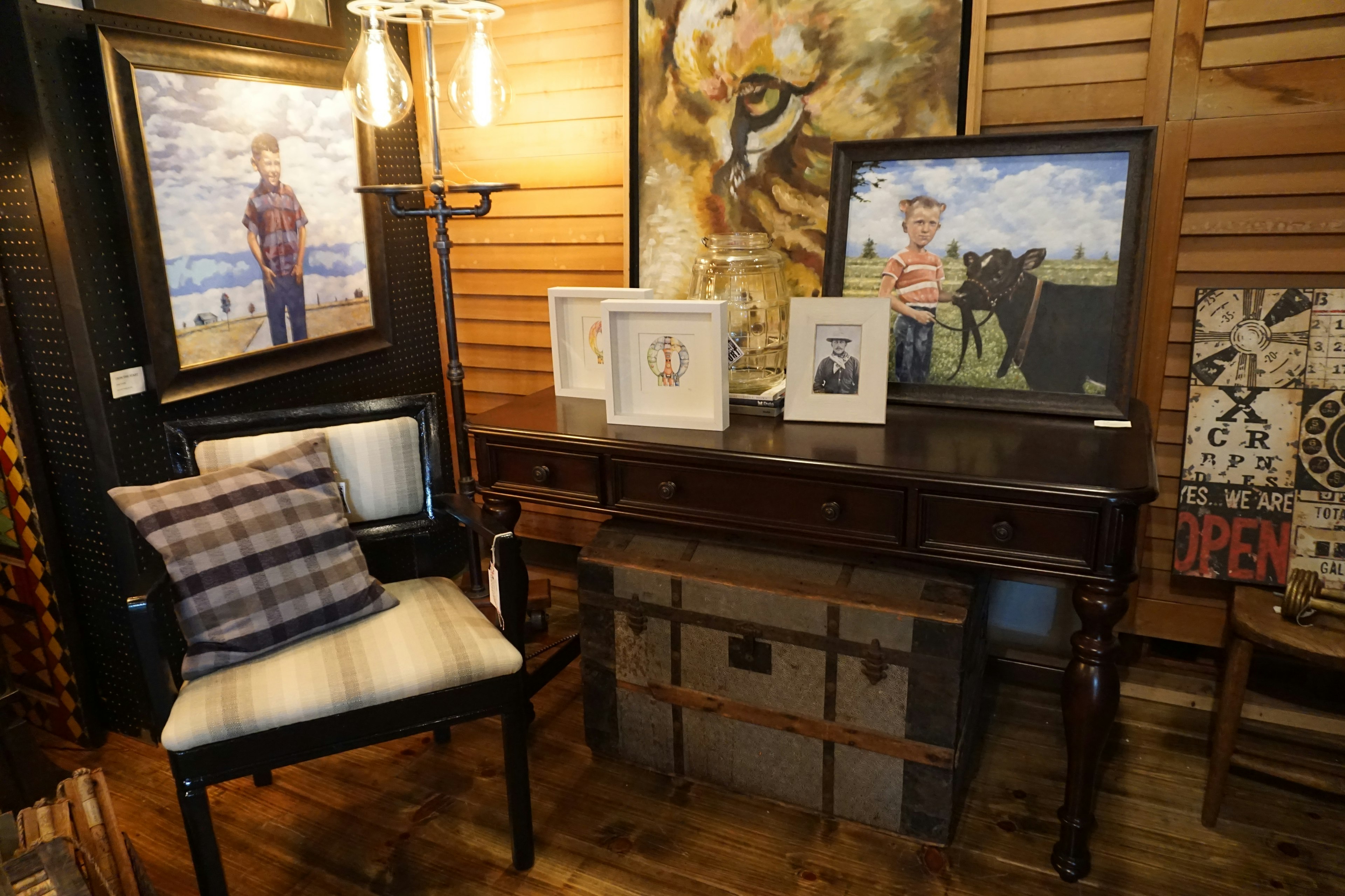 Escena interior con mesa de madera y silla con pinturas y fotografías en la pared