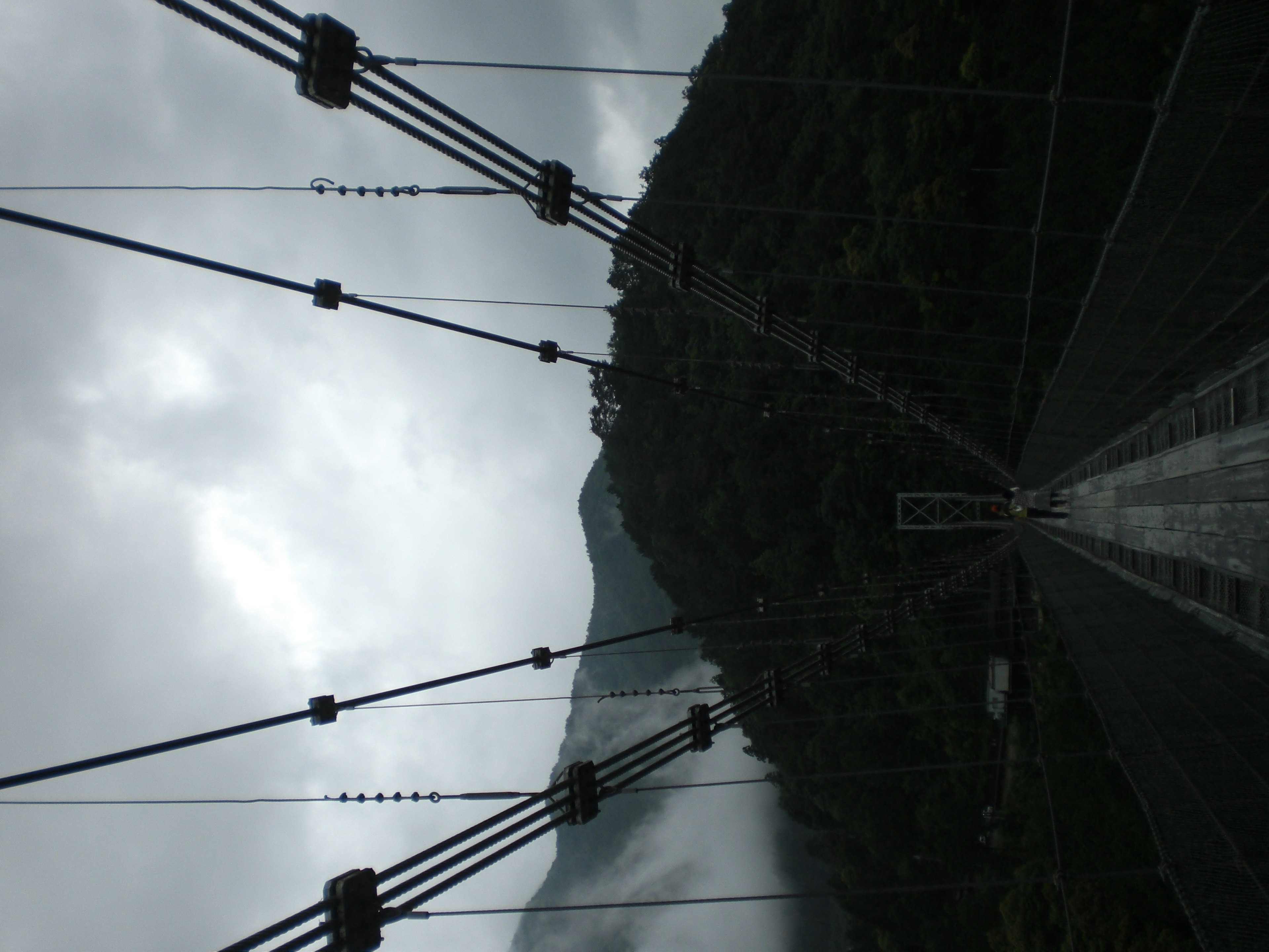 Cables de puente colgante con vista a la montaña bajo un cielo nublado