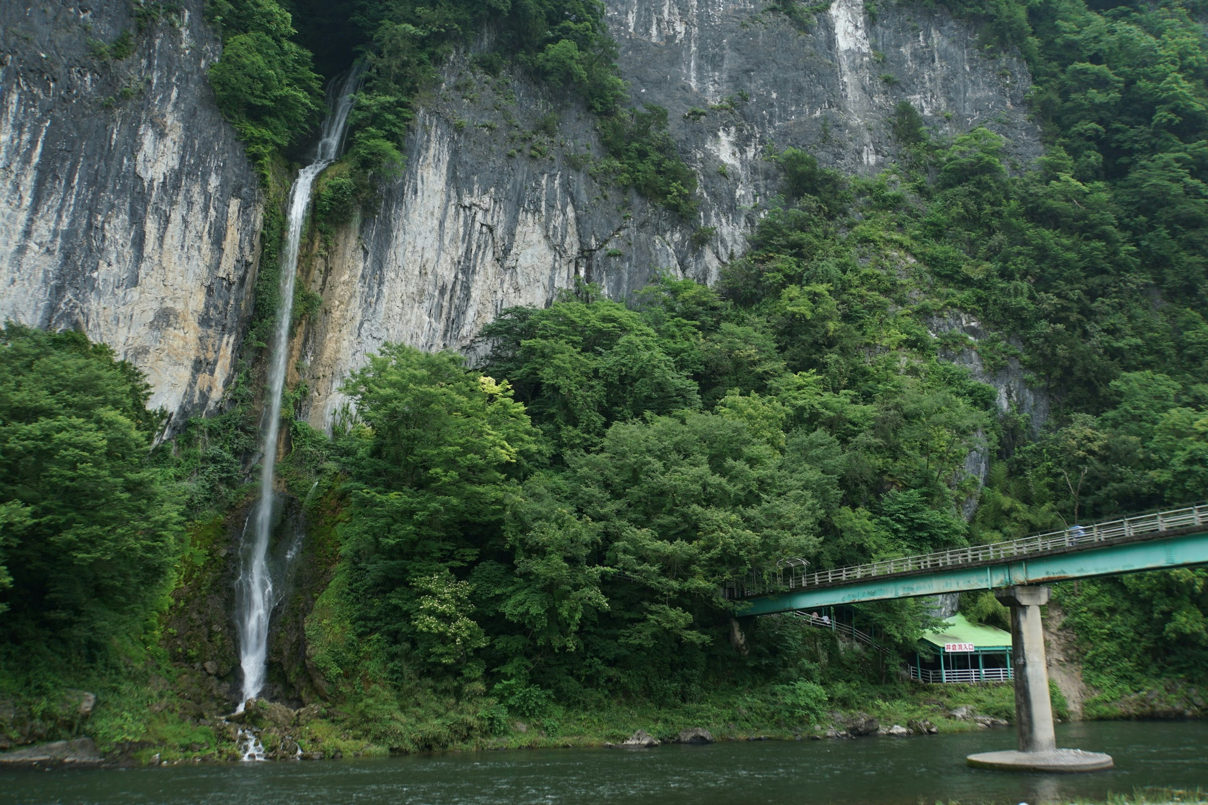 Pemandangan indah air terjun dikelilingi pepohonan hijau dengan jembatan