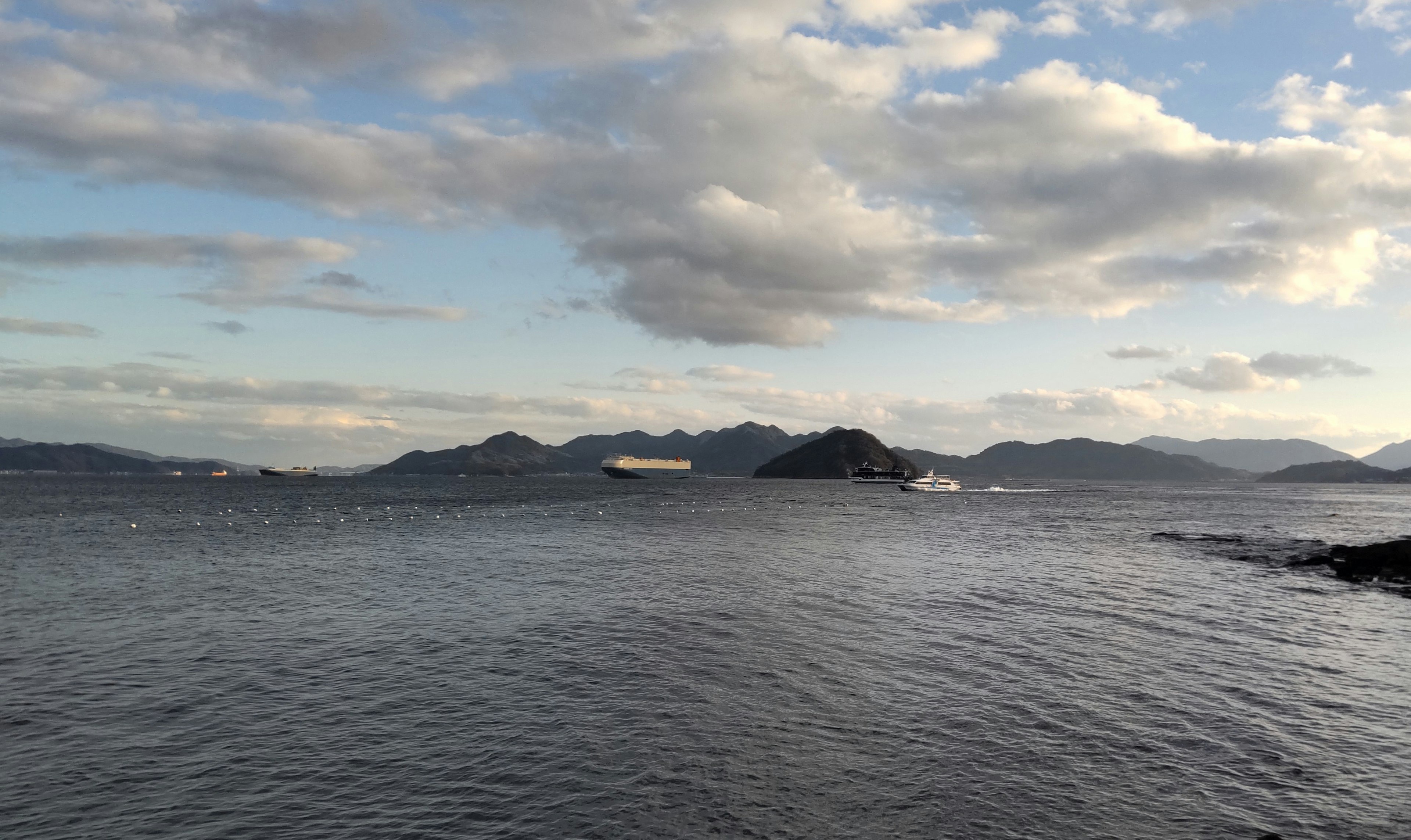 Pemandangan laut dan pegunungan dengan langit biru dan awan